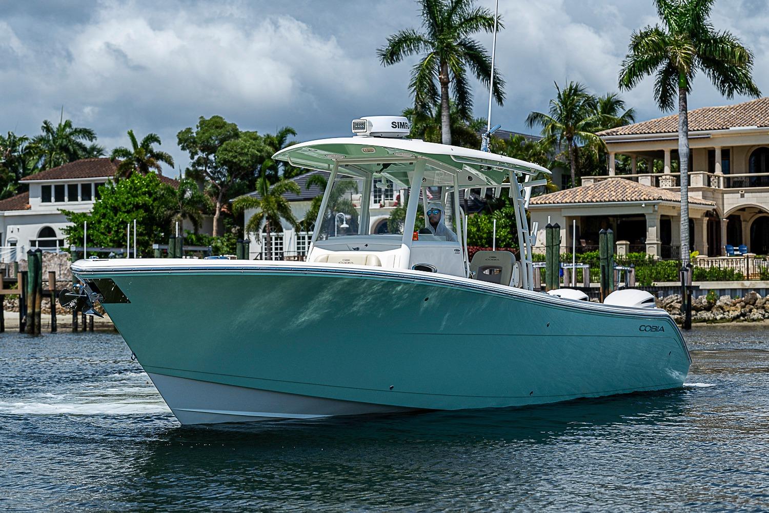 2019 Cobia 320 Center Console boat cruising near waterfront homes.