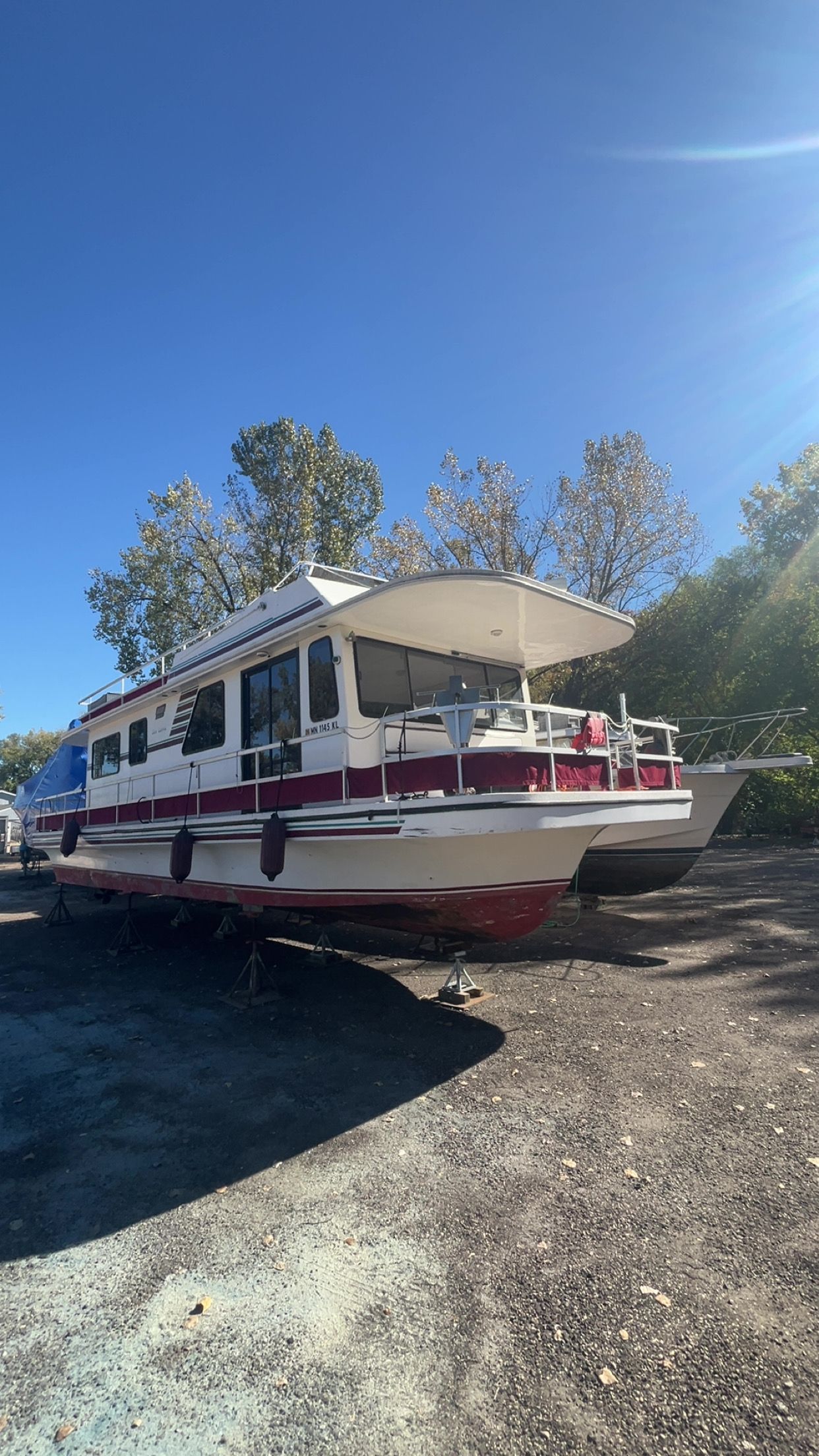 A 1995 Gibson Executive houseboat is on land, surrounded by trees and clear sky.