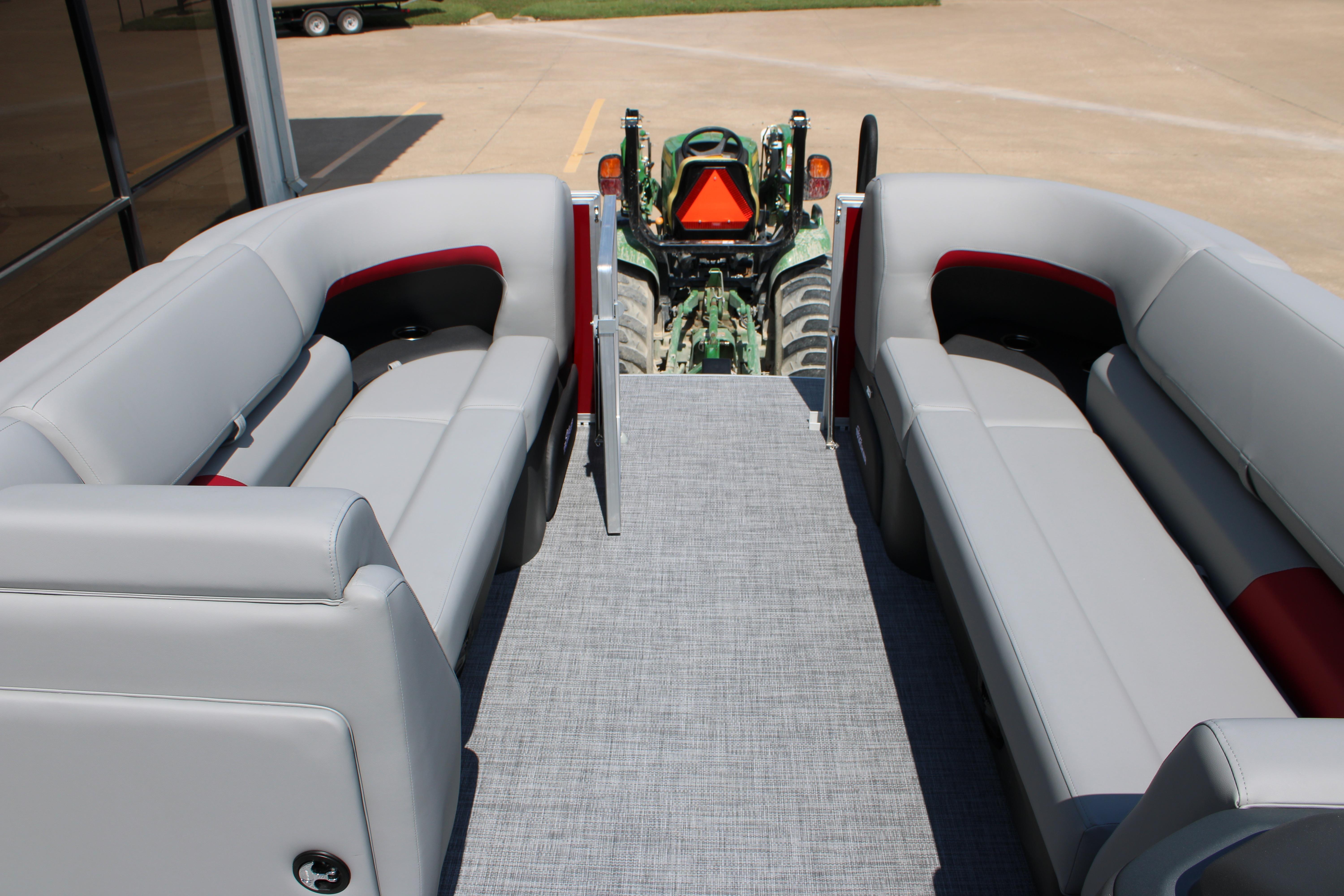 2026 Sun Tracker Party Barge 20 DLX interior with gray seating and tractor in background.