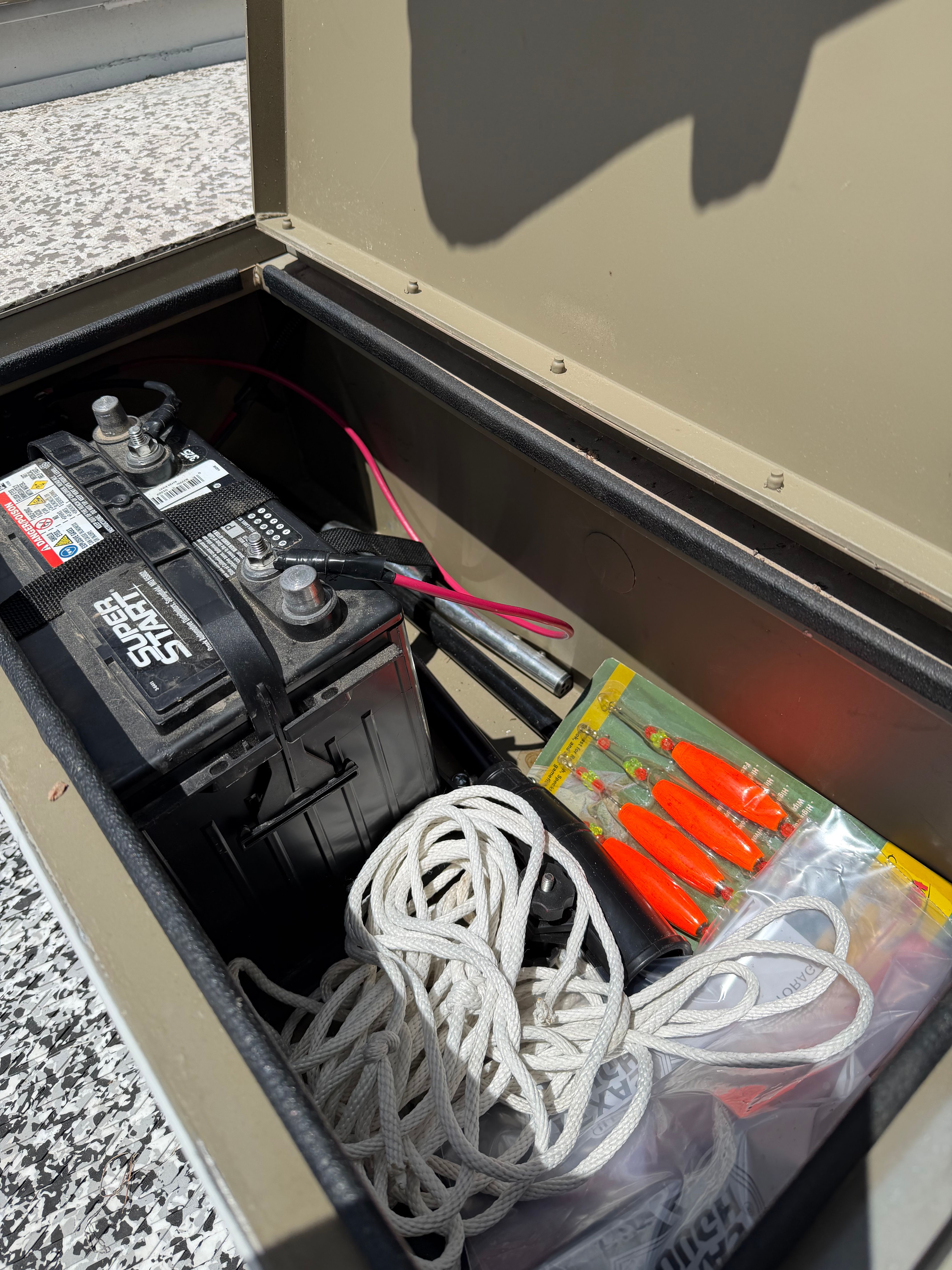 Boat storage with battery, rope, and fishing gear.