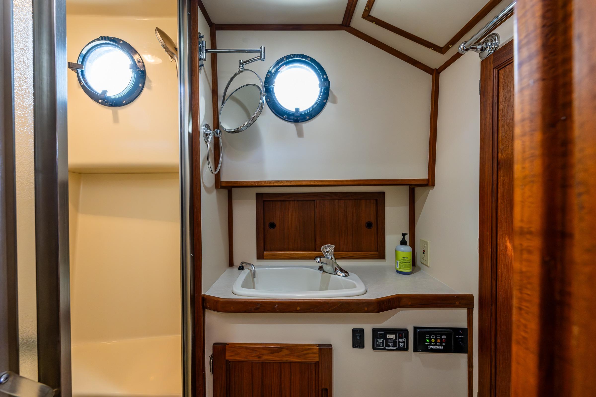 2003 Nordic Tug 37 bathroom with sink, porthole windows, and wooden cabinetry.