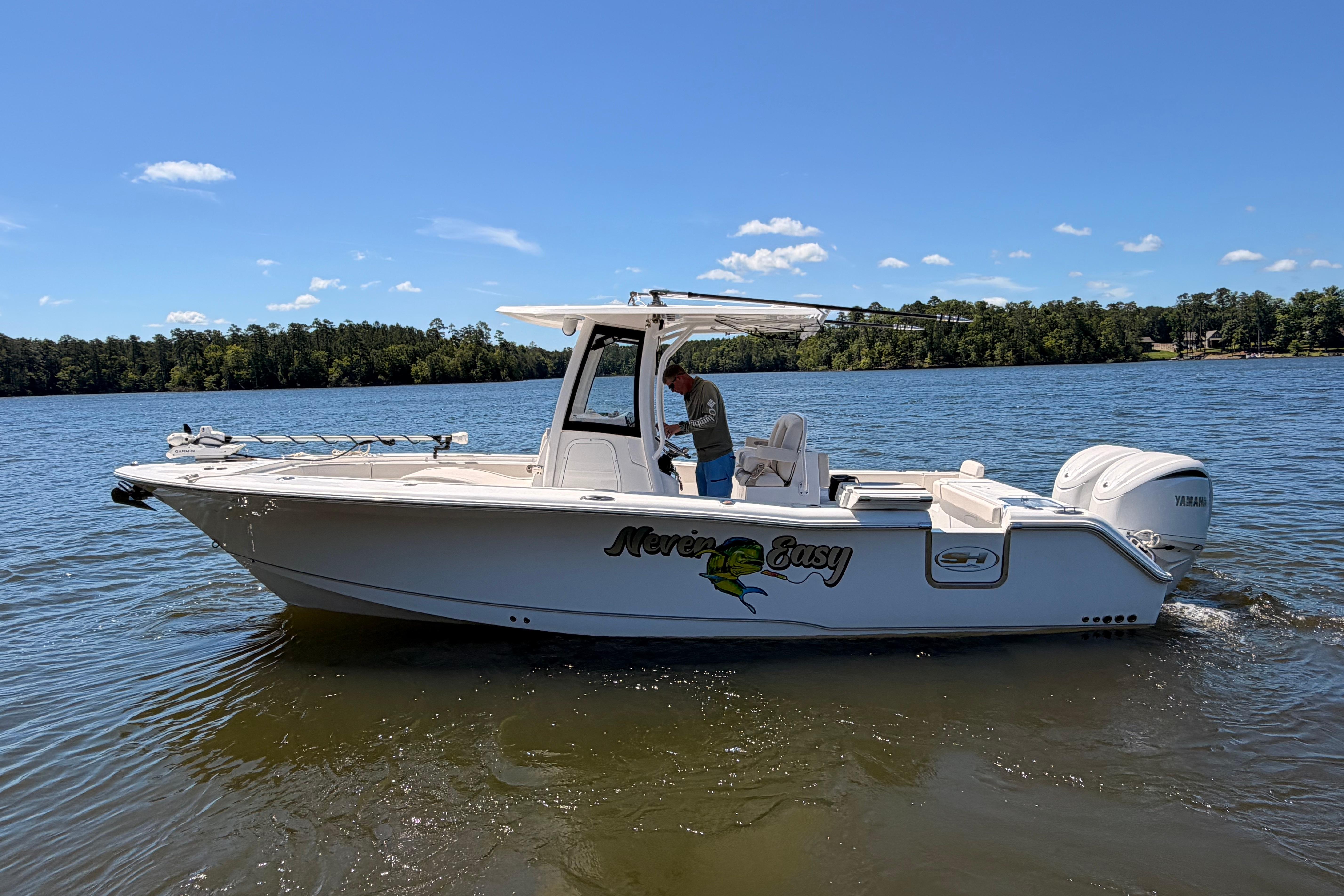2024 Sea Hunt Gamefish 27 Coffin Box boat on a serene lake under a clear blue sky.