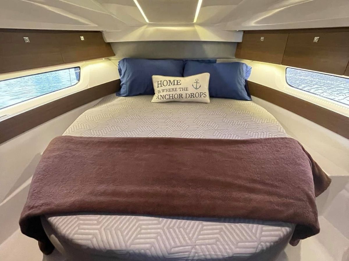 The interior of a 2019 Jeanneau NC 895 features a cozy bedroom with a decorative pillow.