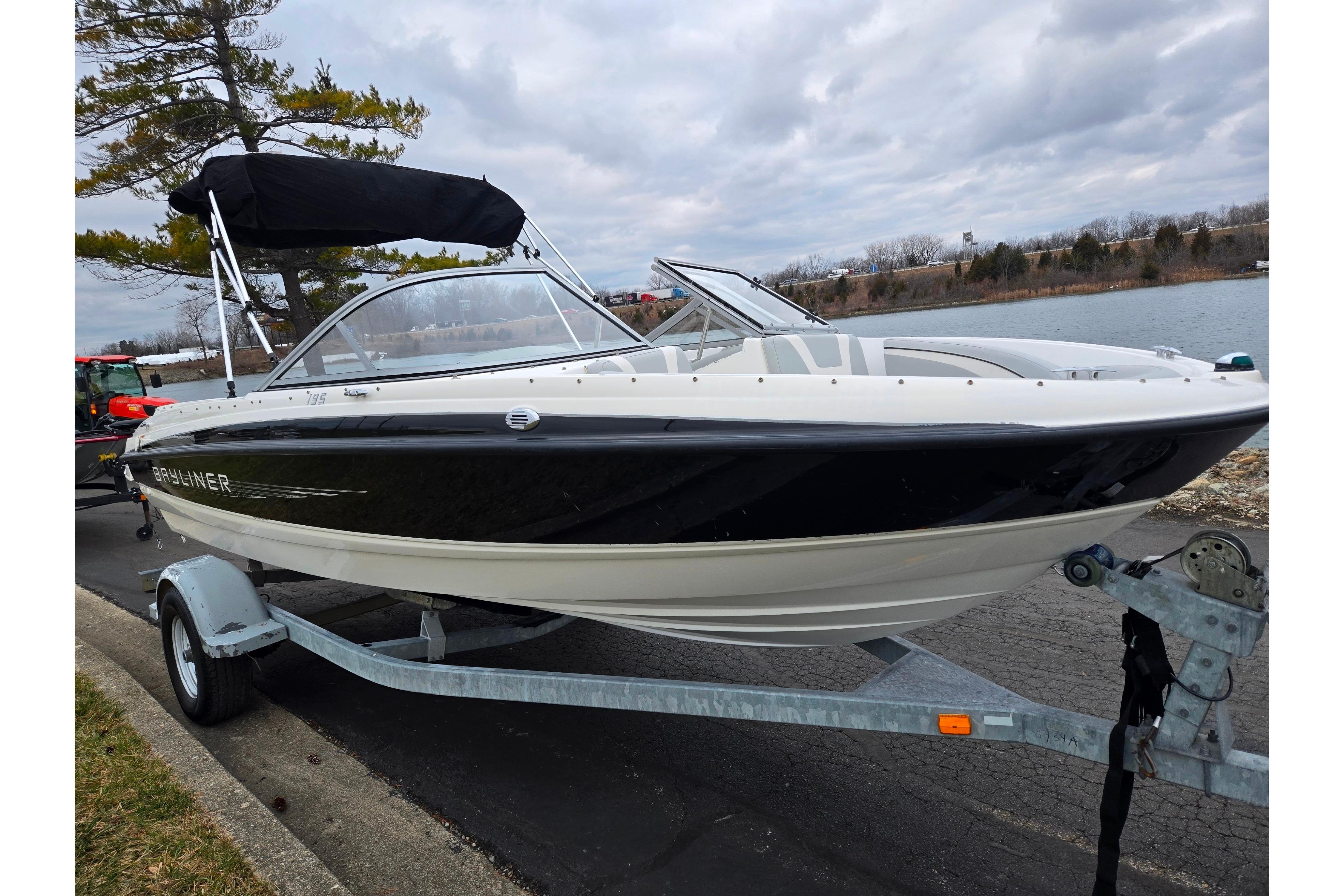2011 Bayliner 195 boat on trailer by lakeside, under cloudy sky.
