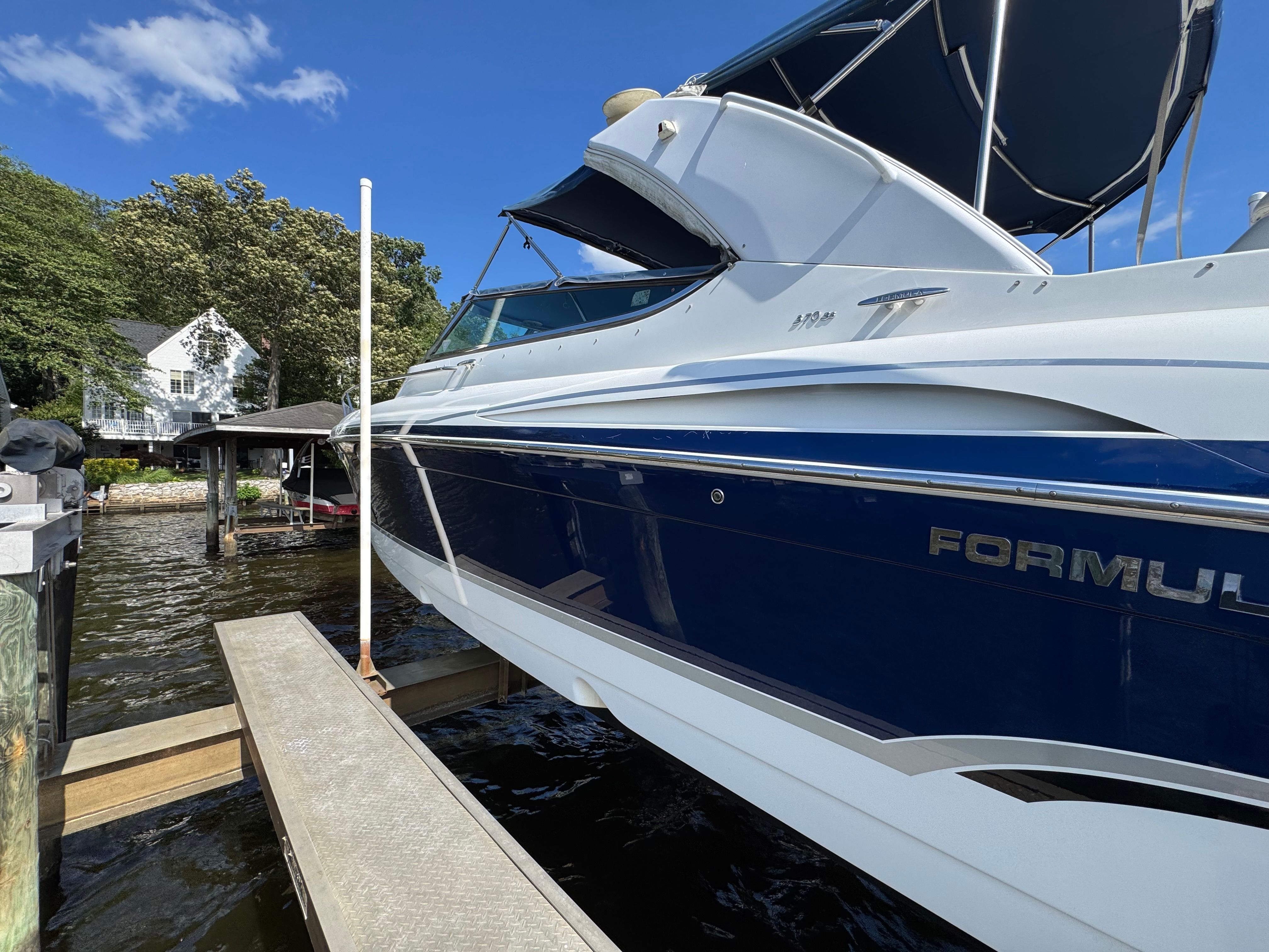 A blue and white boat docked, surrounded by trees and a house.
