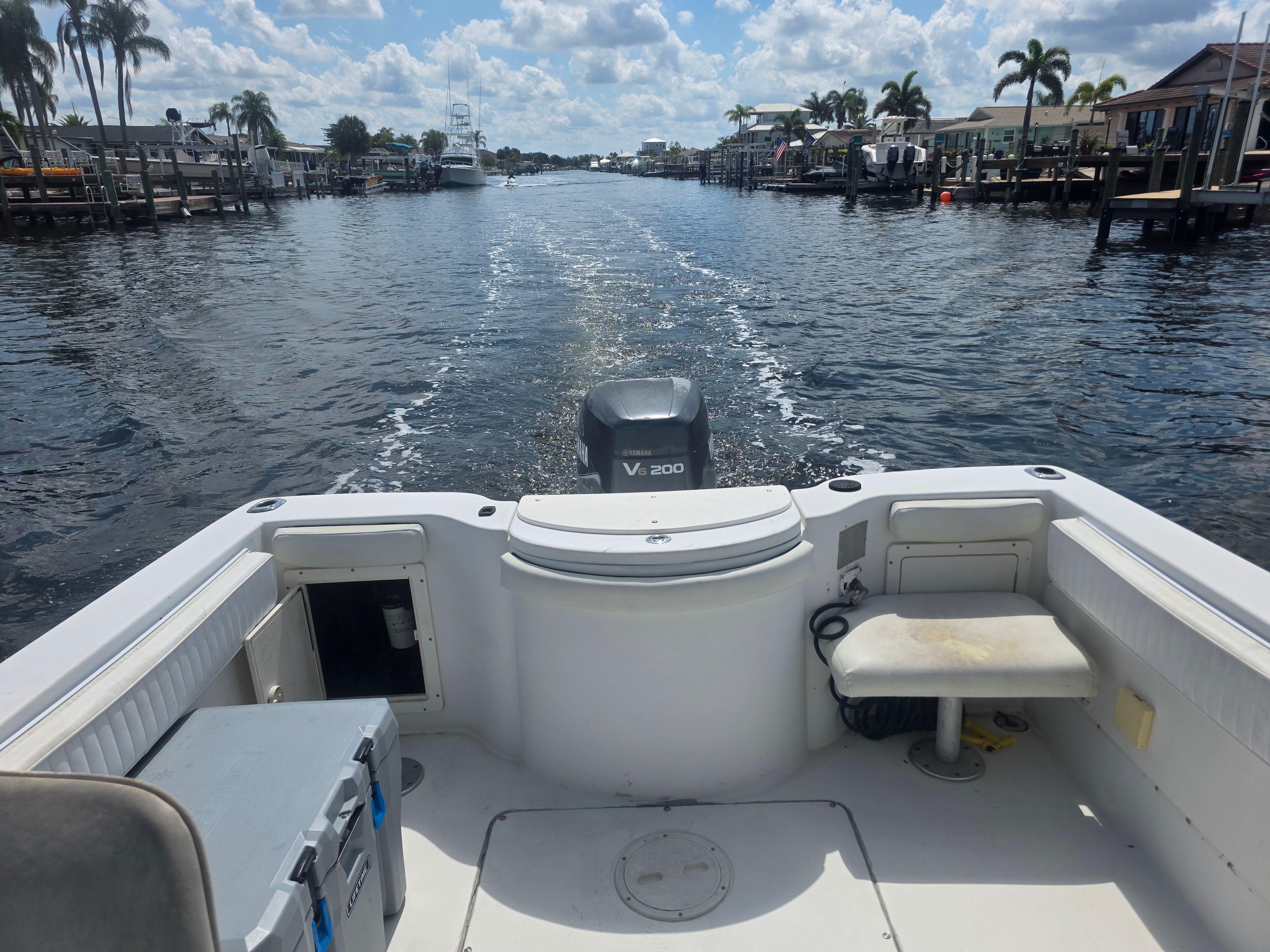 The boat is cruising on a calm waterway with palm trees and houses along the shore.