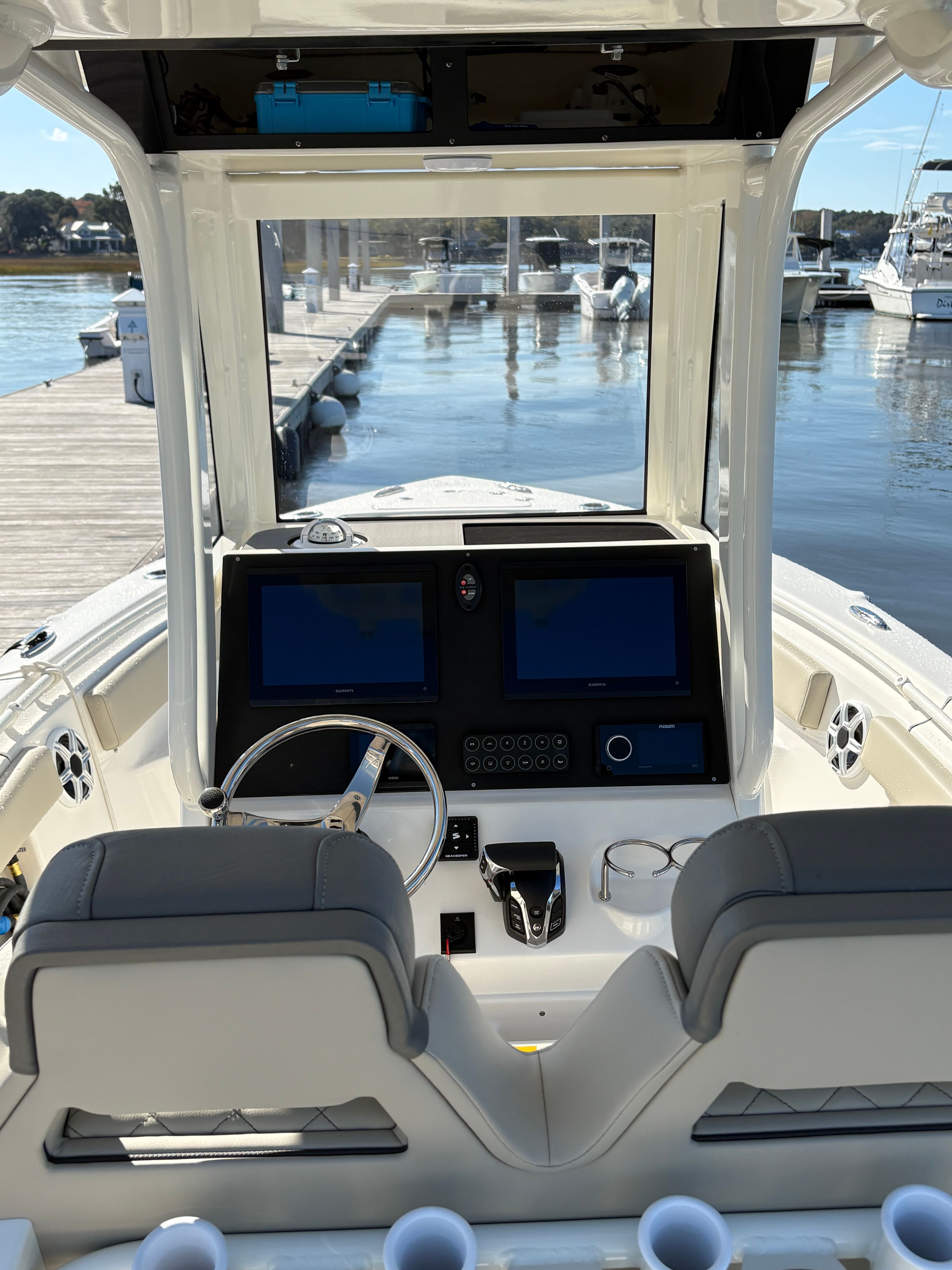 The image shows the cockpit of a Key West 239 FSR boat. It features two seats, a modern dashboard with multiple screens, and a steering wheel. A calm marina is visible in the background.