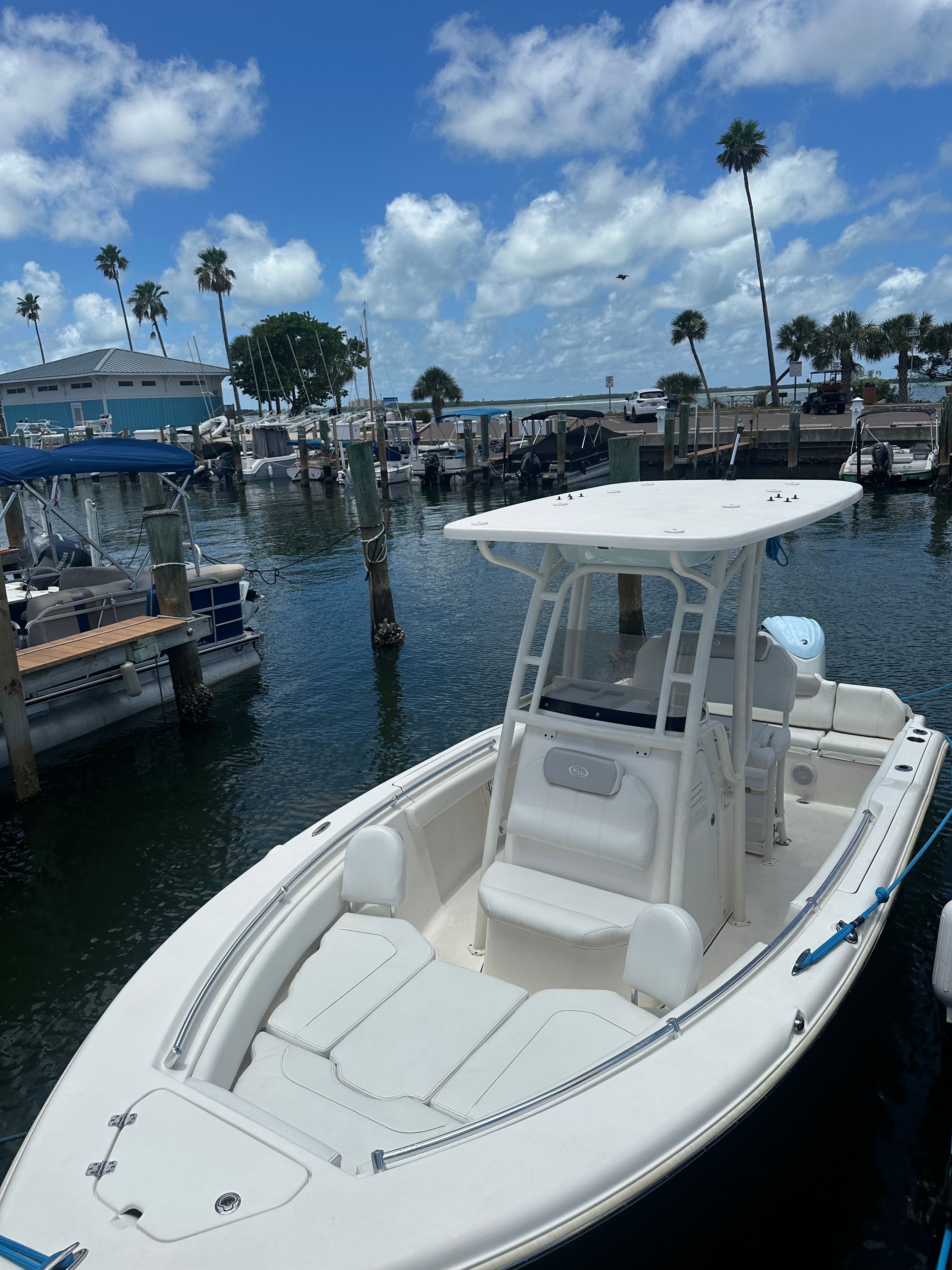 A white boat is docked in a calm harbor with palm trees in the background.