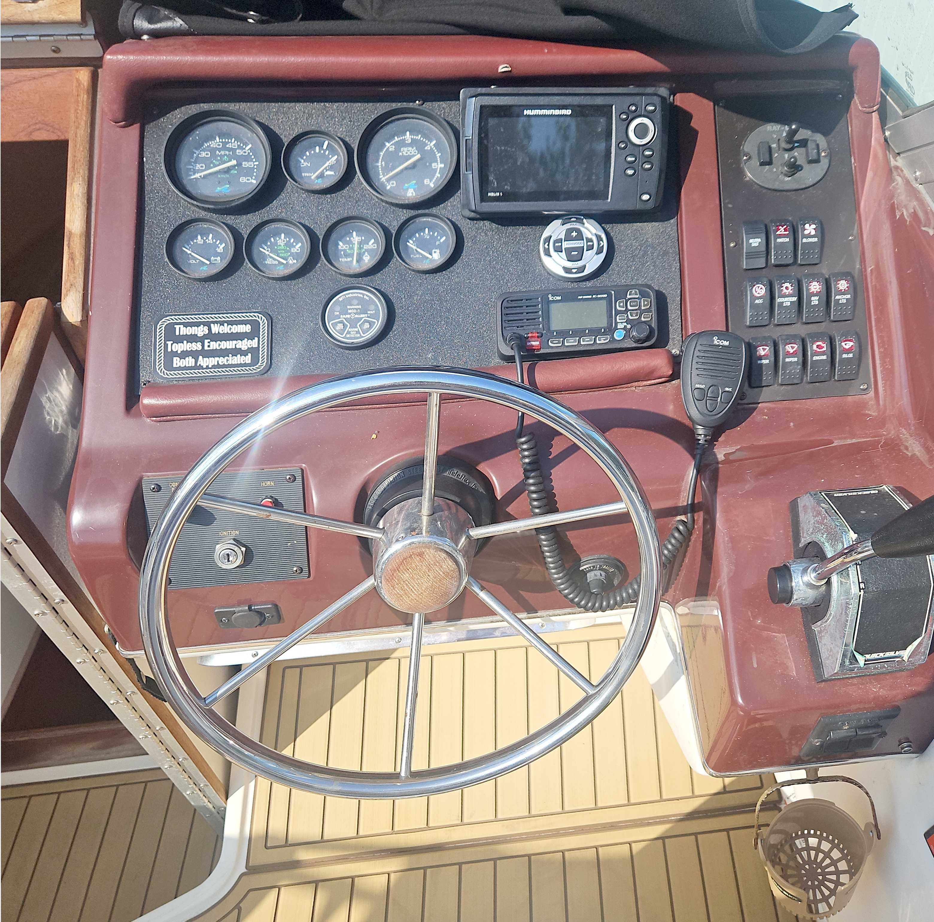 The image shows a boat's helm with a large steering wheel and various instruments.