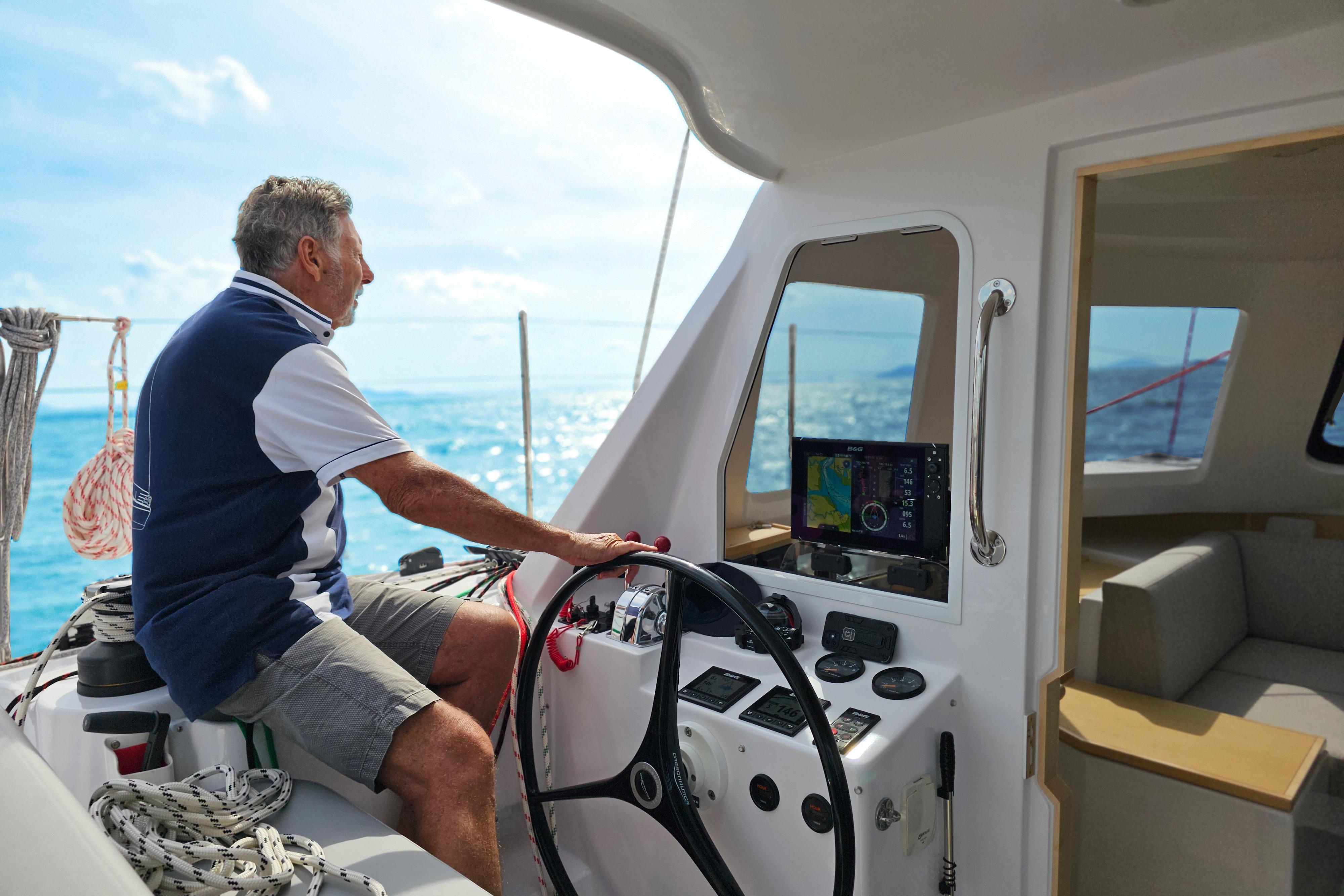 Man steering 2026 Seawind 1160XL catamaran on open sea, sunny day.