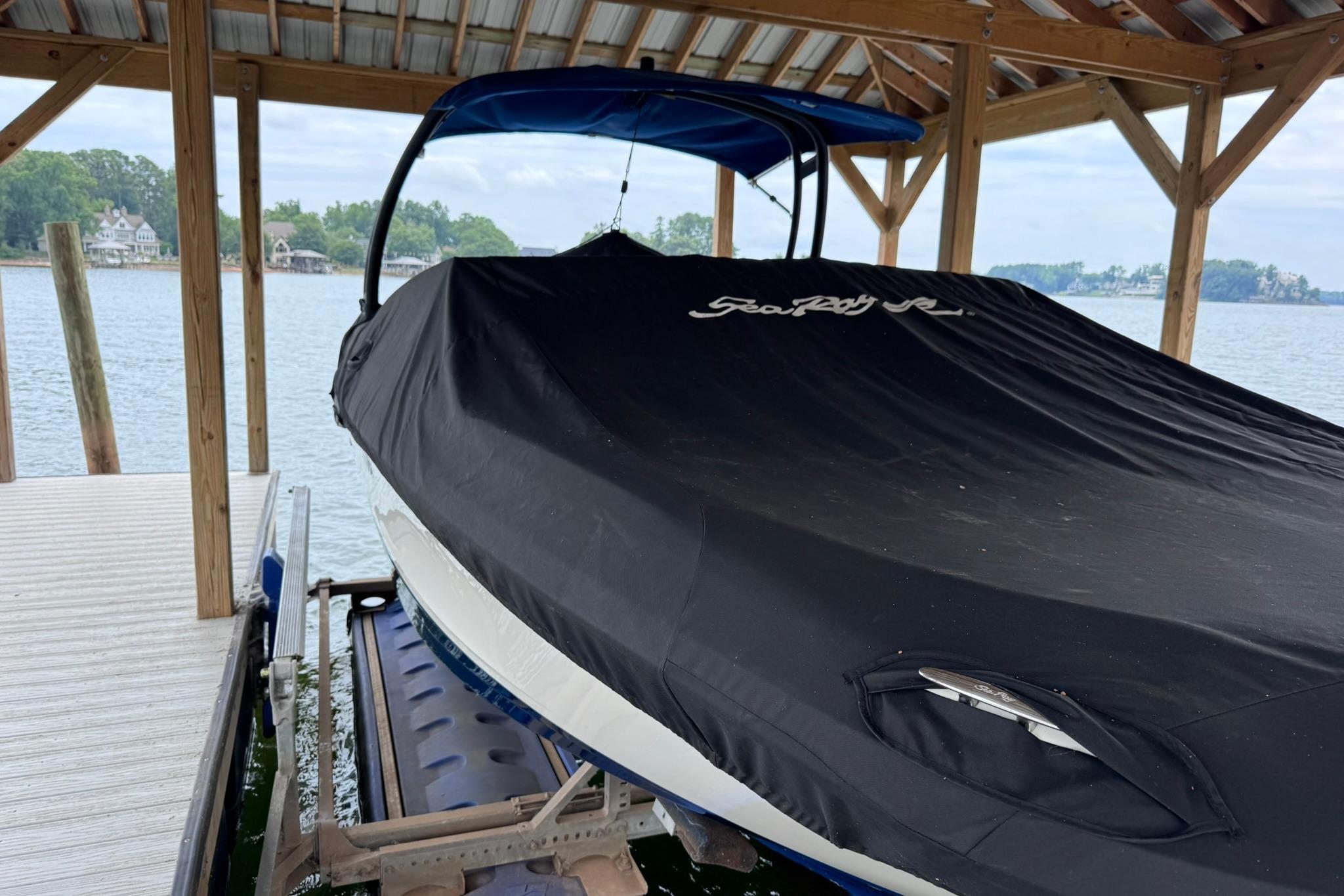 2021 Sea Ray SPX 230 boat covered and docked under a wooden shelter by the lake.