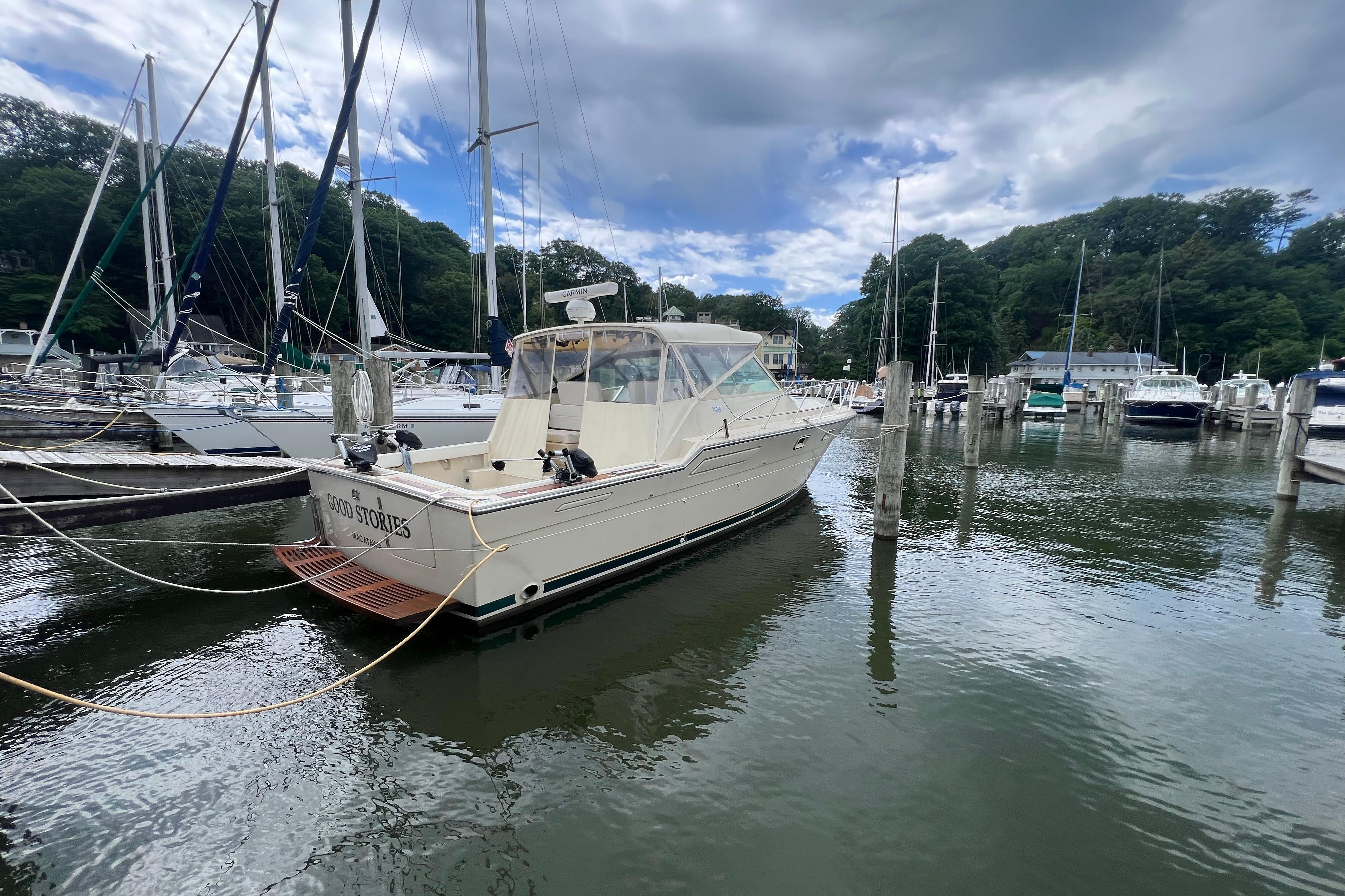1985 Tiara 36 OPEN yacht docked in a marina with sailboats and trees.