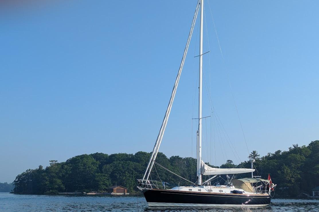 Sailboat Tartan 4300 (2009) on calm water near a forested shoreline.