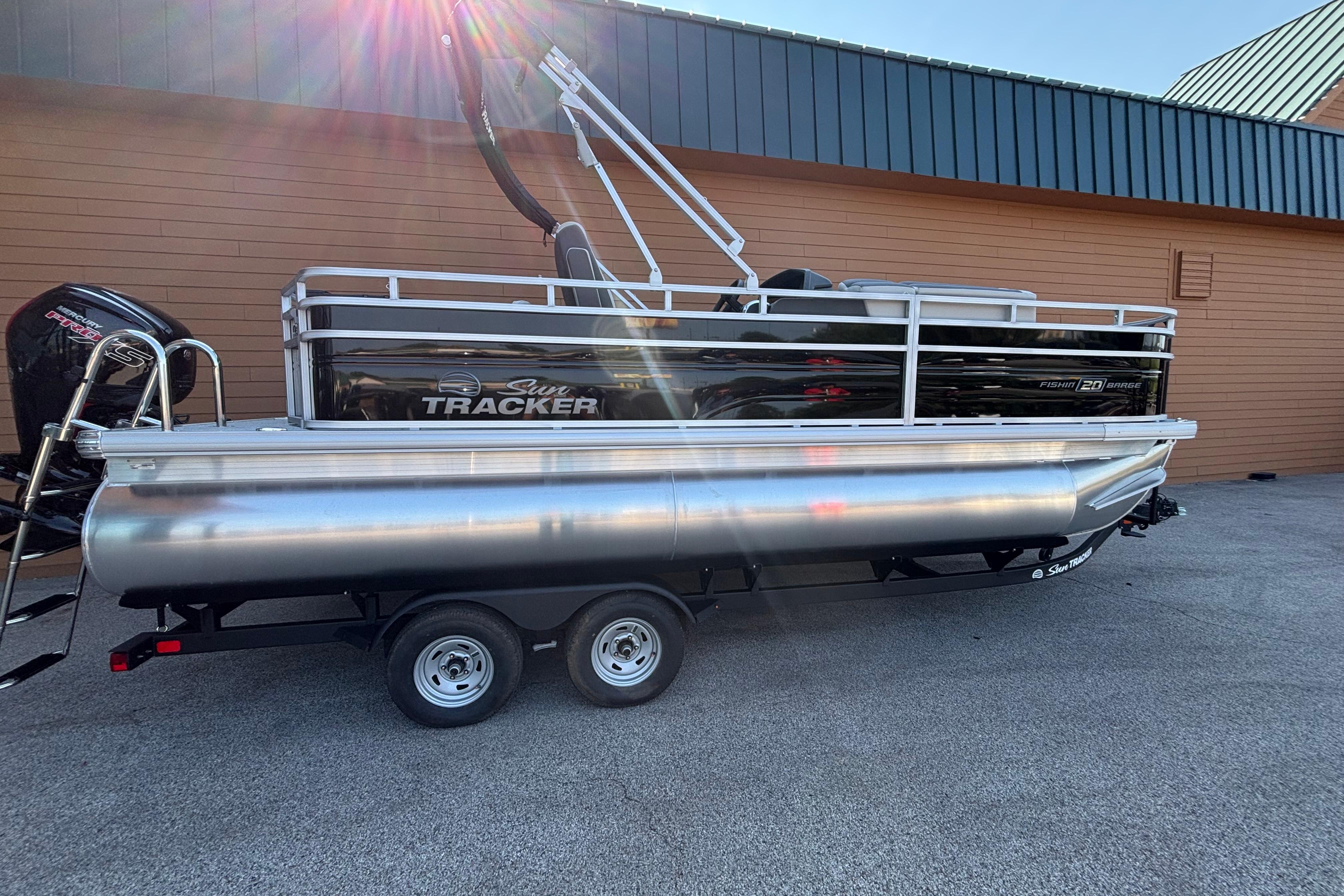 2026 Sun Tracker Fishin' Barge 20 DLX pontoon boat on trailer, parked outdoors.