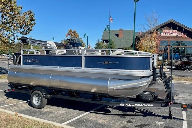 2026 Sun Tracker Bass Buggy 18 DLX pontoon boat on trailer in parking lot.