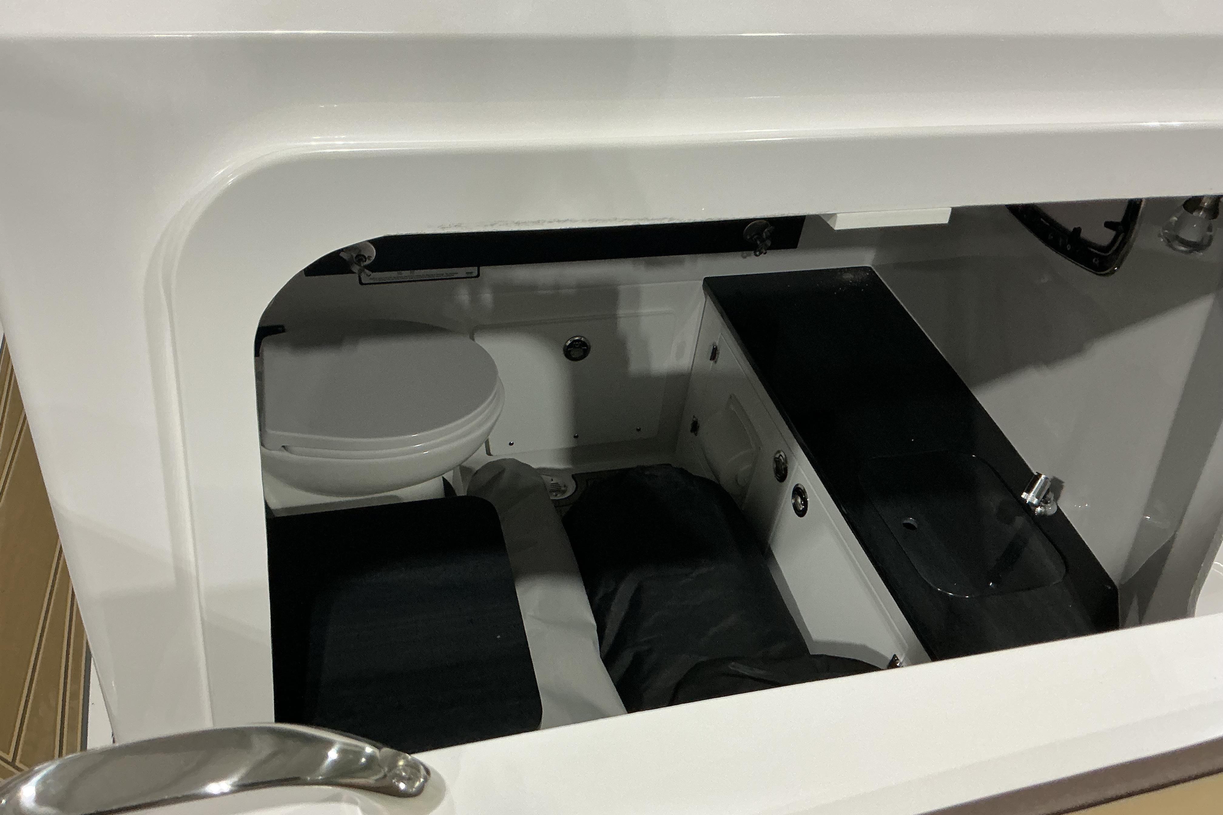 Interior cabin view of 2026 Monterey Elite 25 OB boat, featuring a compact toilet and sink.
