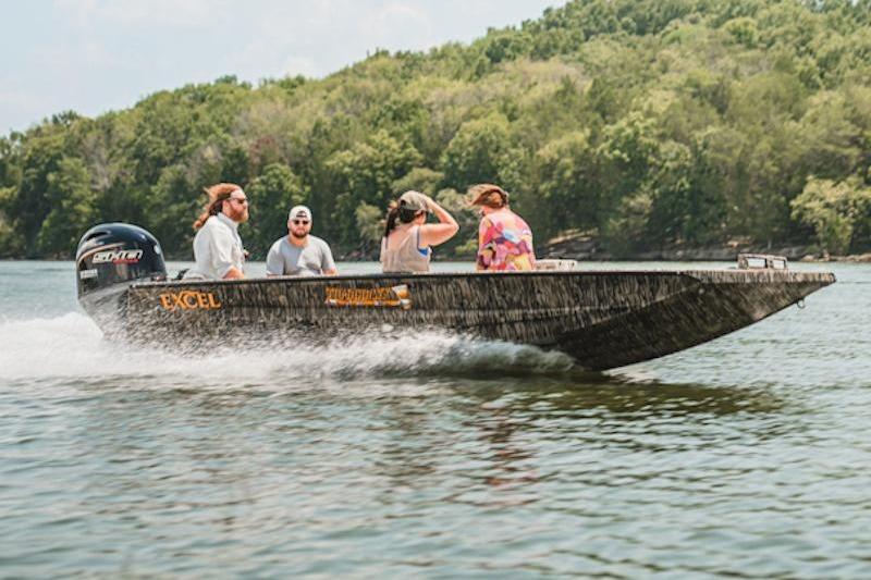 2026 Excel 183 Tomahawk boat cruising on a lake with four passengers, surrounded by lush greenery.