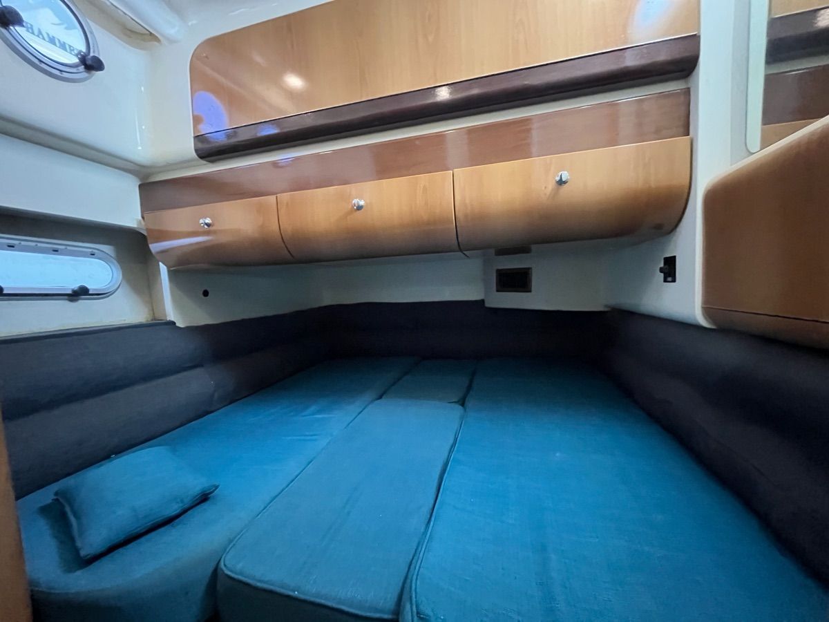 The 1999 Sealine F44 cabin features a cozy bed with blue cushions and wooden cabinets.