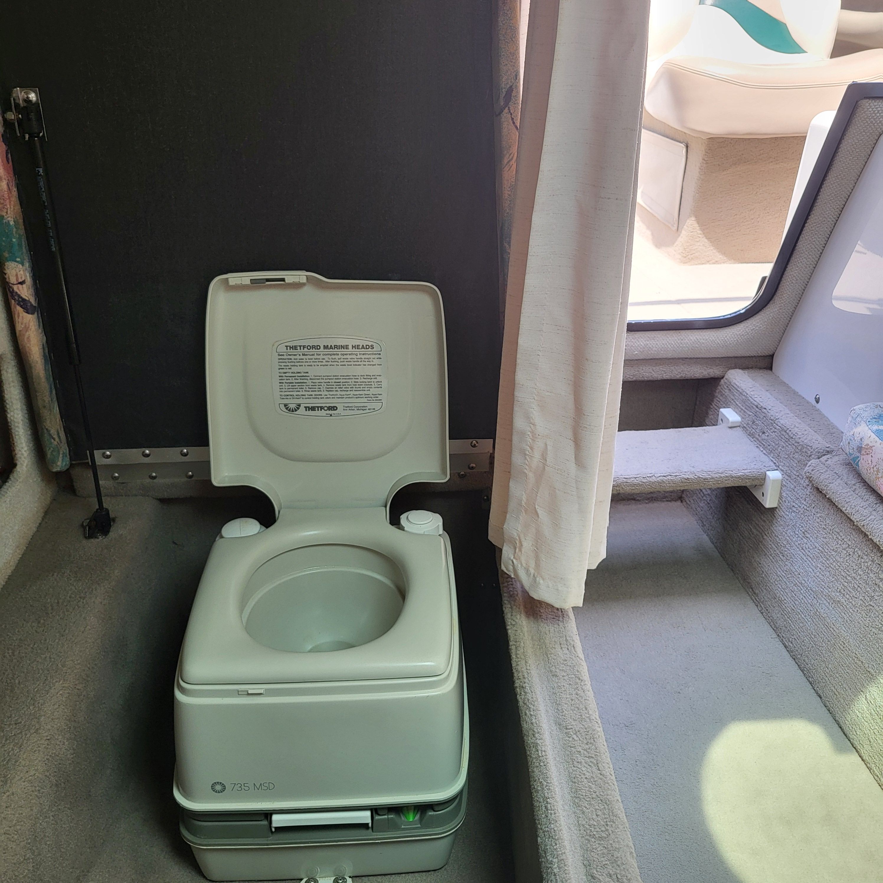 Interior of a 1996 Four Winns 245 Sundowner with a portable toilet and carpeted floor.