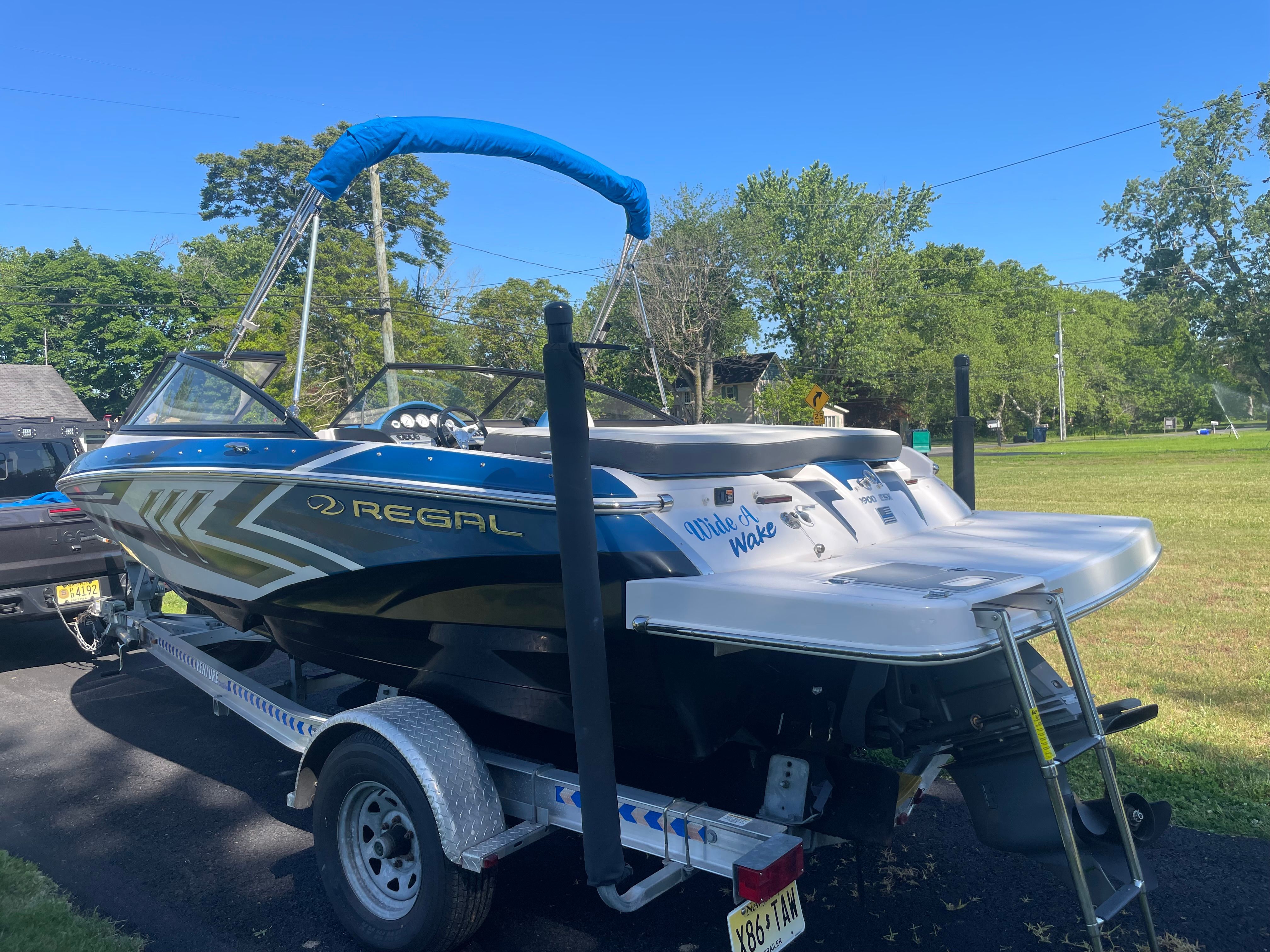 A 2016 Regal 1900 ESX Bowrider on a trailer, surrounded by trees and grass.