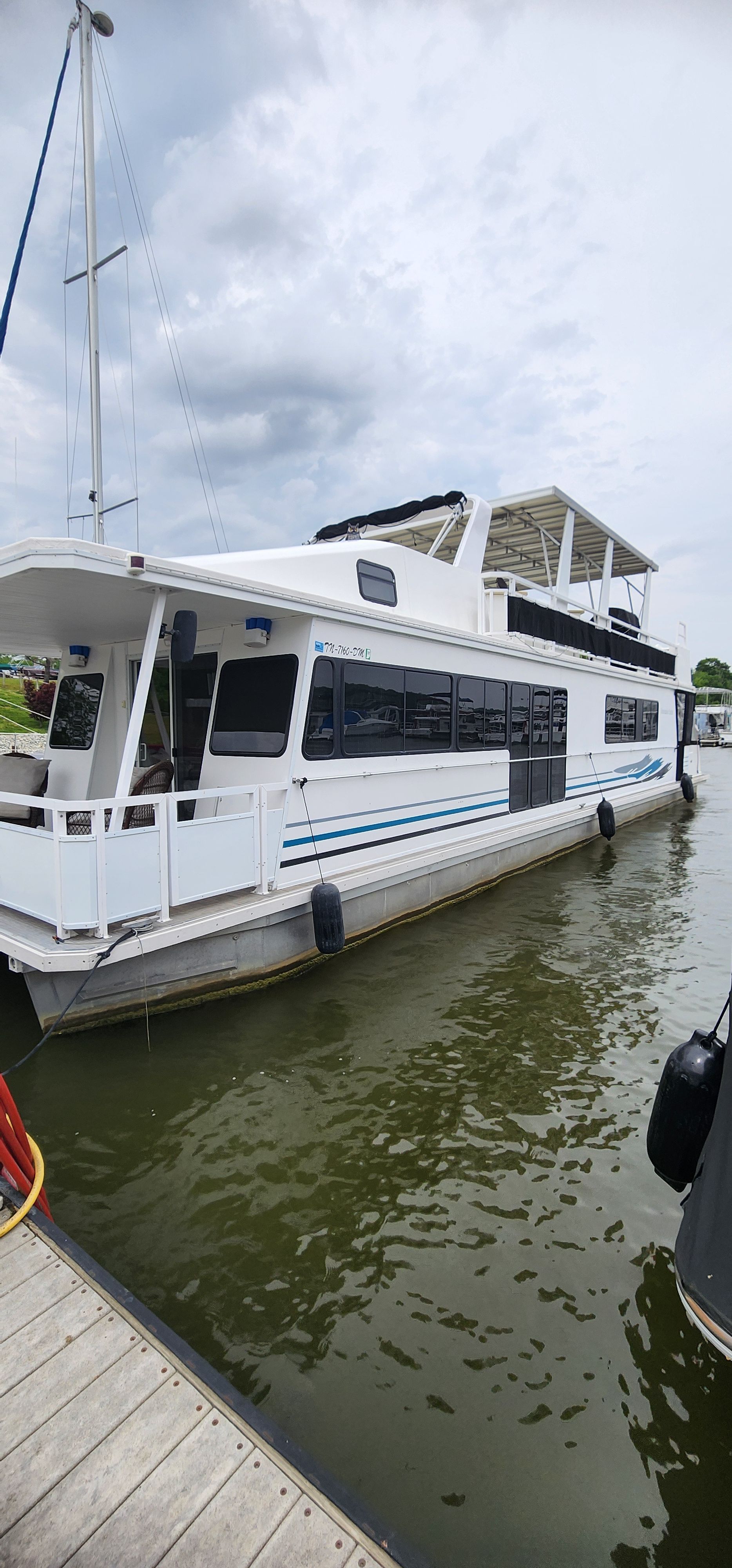 A large two-level houseboat is docked at a pier.