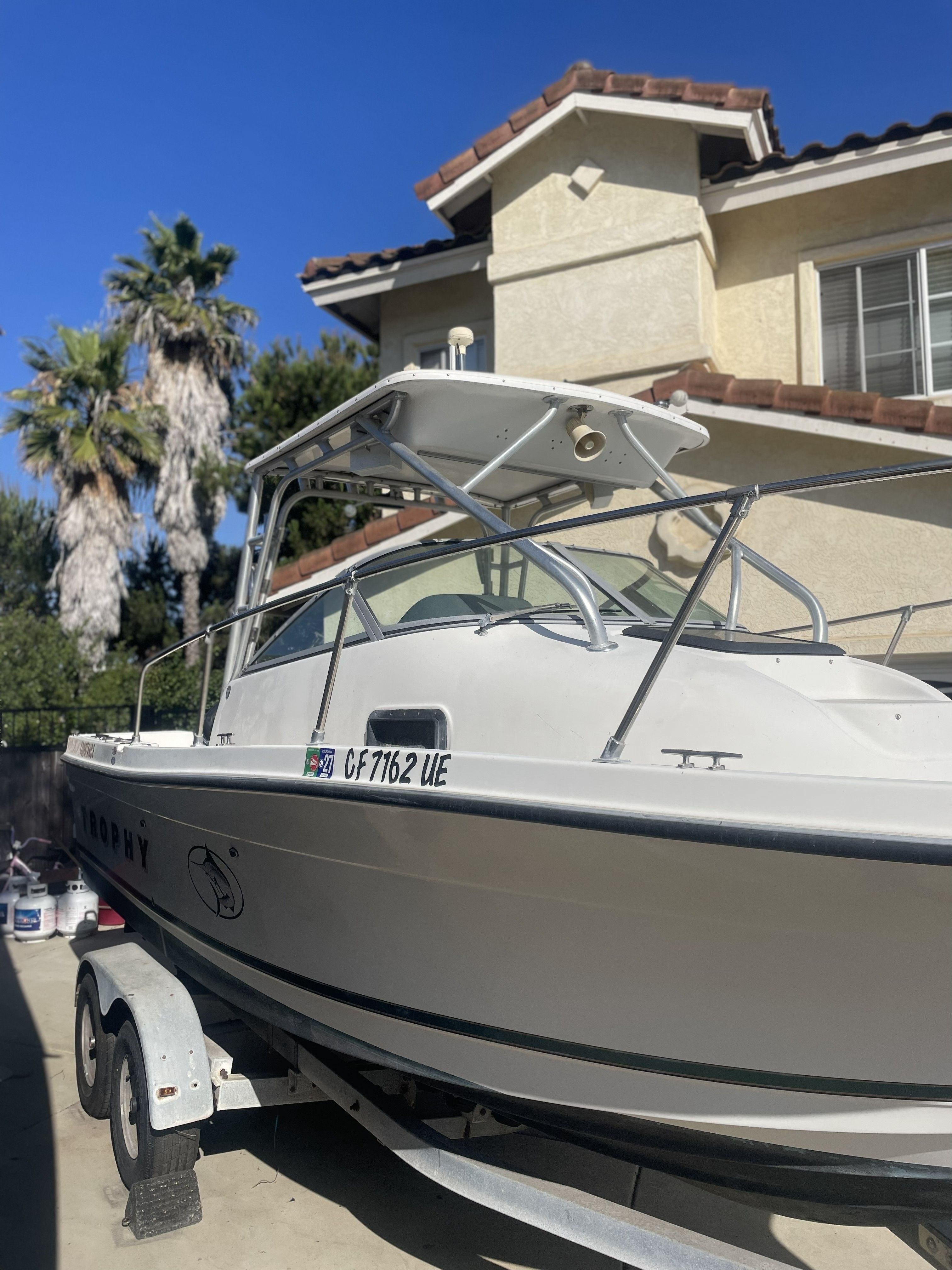 A white Bayliner Trophy boat on a trailer in front of a house.