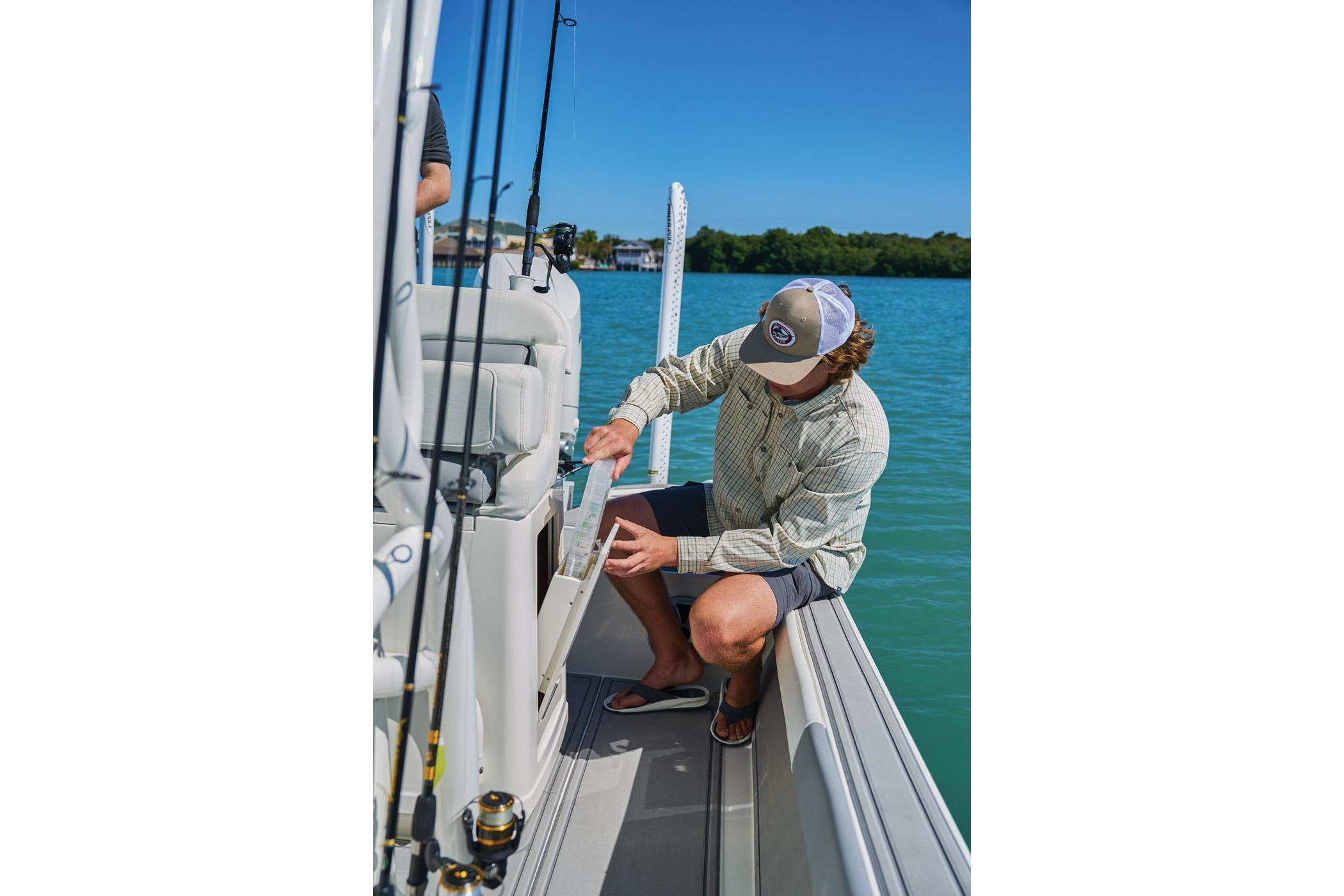Man organizing fishing gear on a 2026 Mako 24 APEX boat in sunny waters.