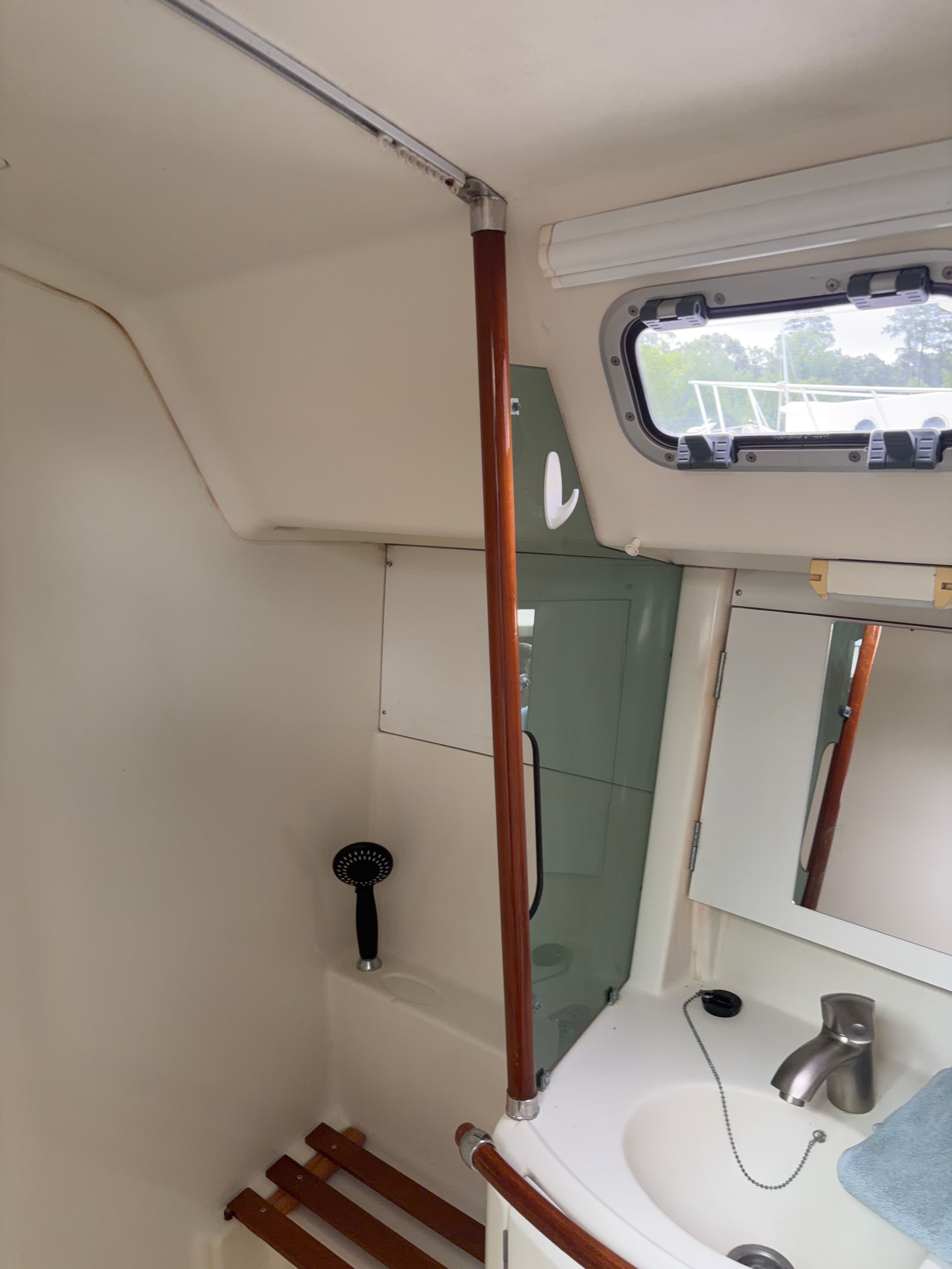 Interior view of a boat bathroom with sink, mirror, and shower.