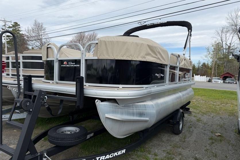 2025 Sun Tracker Party Barge 16 DLX pontoon boat on trailer, covered and parked outdoors.