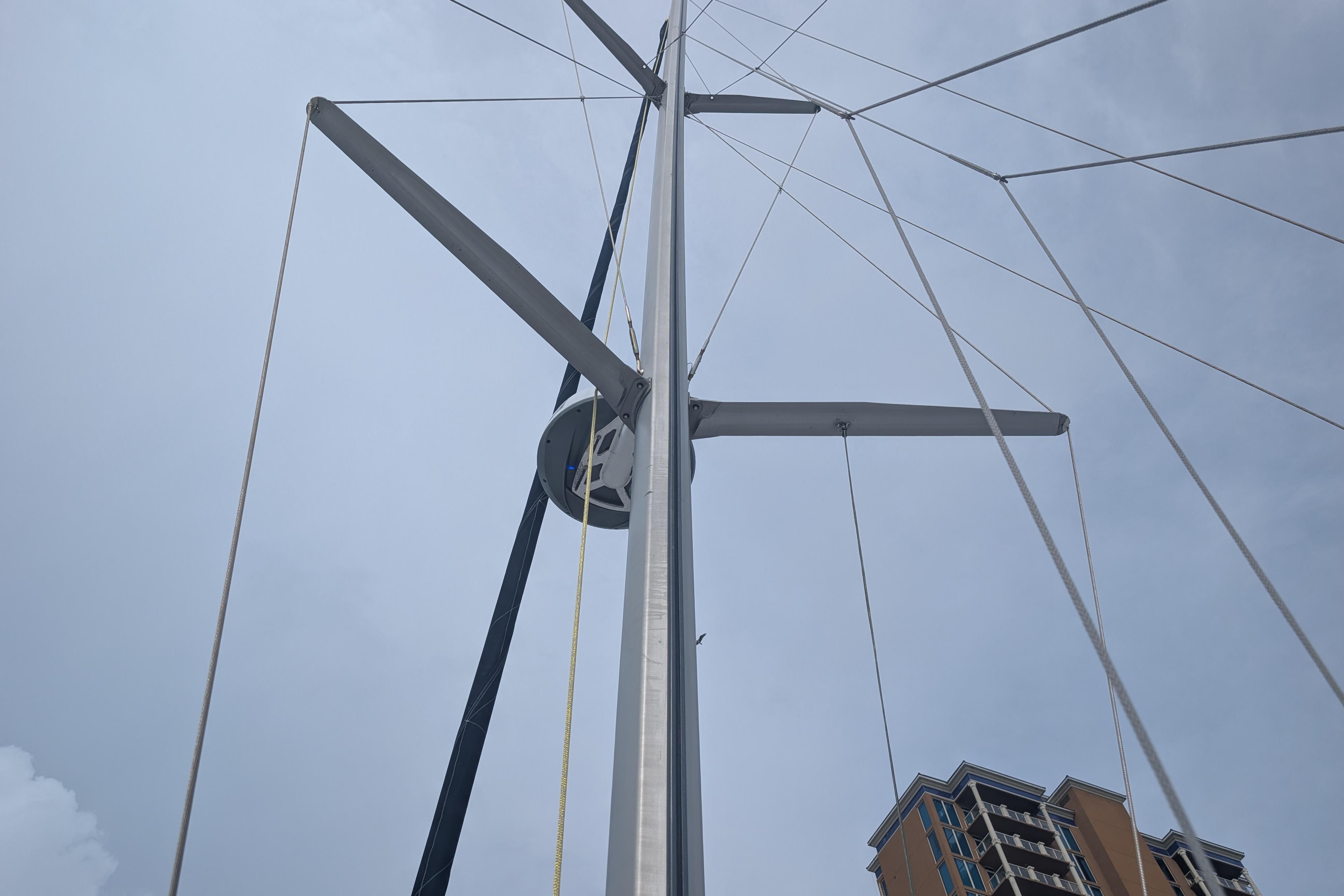 Mast of 1999 Island Spirit 37 sailboat against cloudy sky, with building in background.