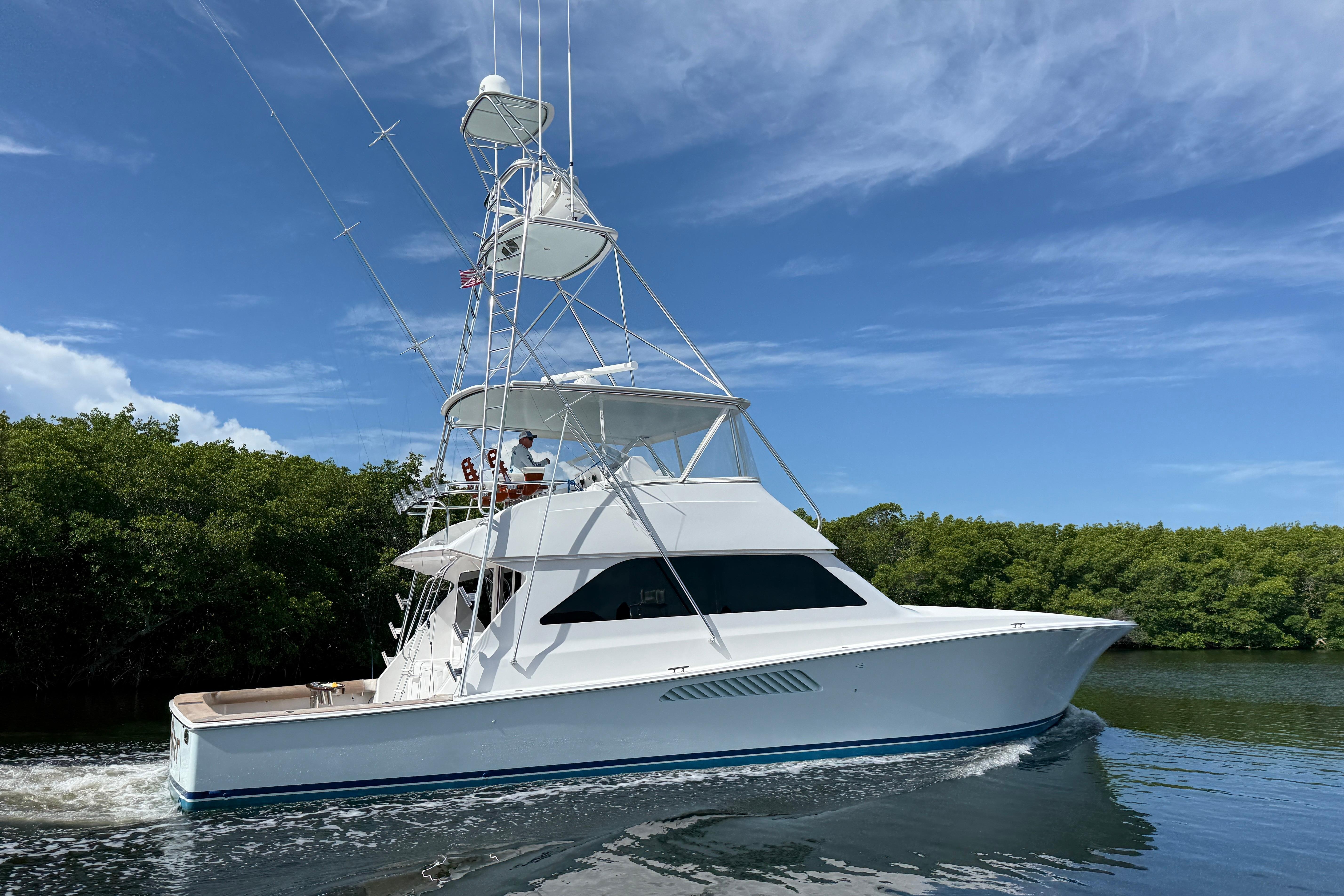 2000 Viking 55 Convertible yacht cruising on a sunny day near lush greenery.