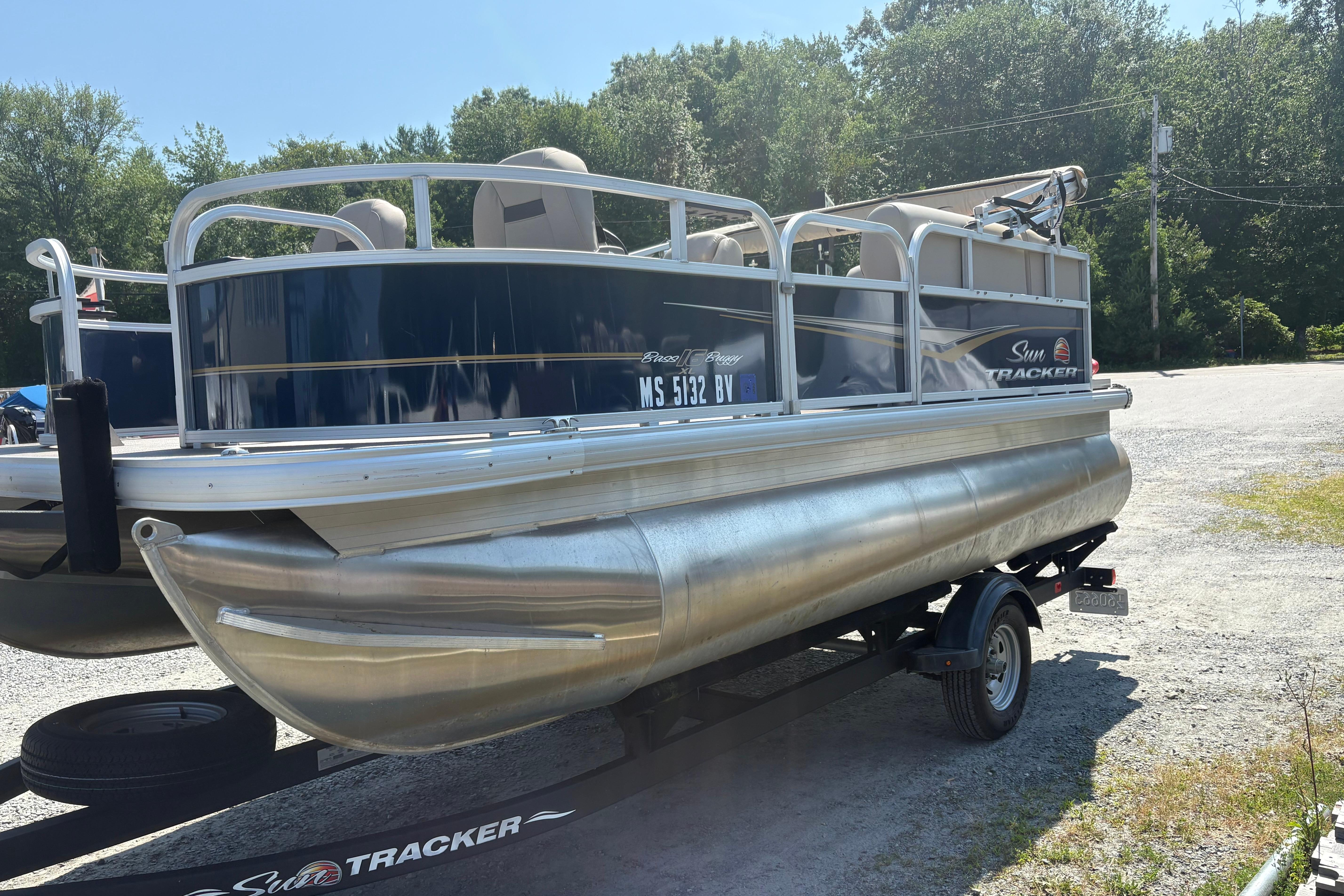 2024 Sun Tracker Bass Buggy 16 DLX pontoon boat on trailer, parked outdoors.