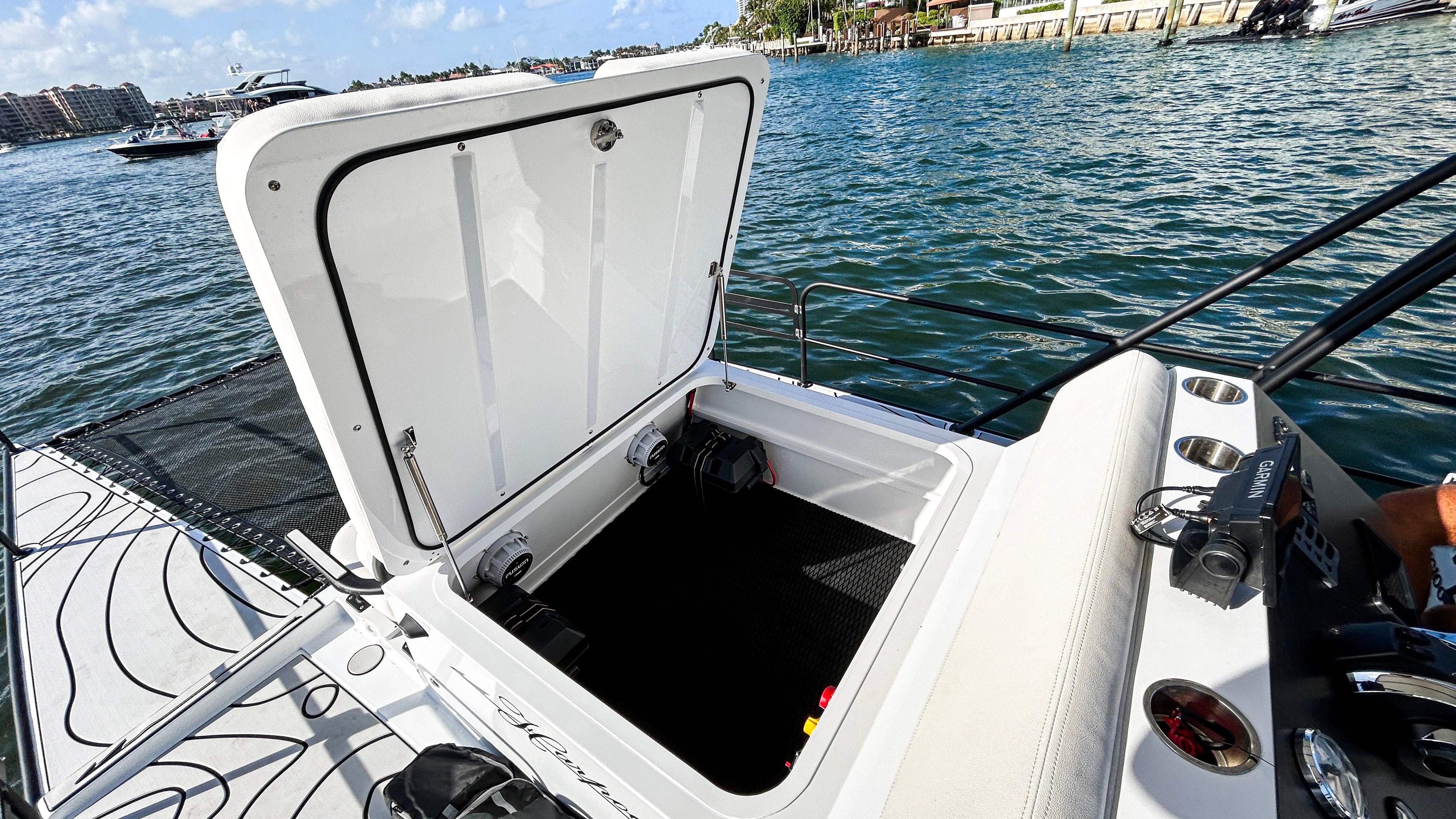 2025 Pontoon Harpoon boat with open storage compartment on a sunny day by the water.