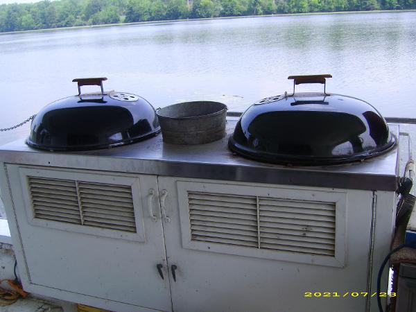 Outdoor grill setup on a Pluckebaum Baymaster boat, 1980 model, by a serene lake.