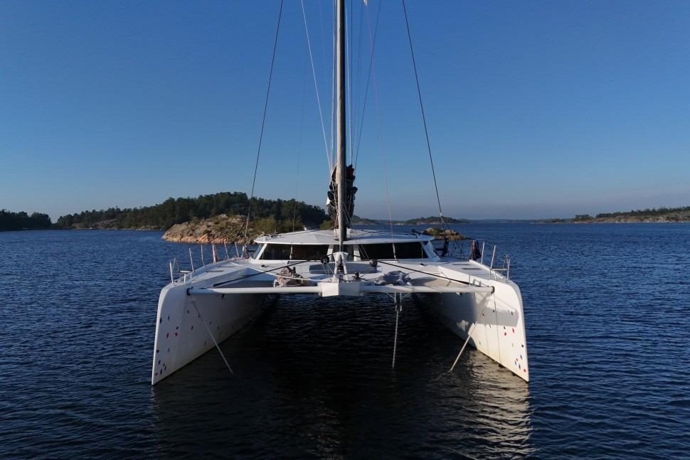 Front view of a 2015 Alibi 65 catamaran sailing in calm waters under a clear blue sky.