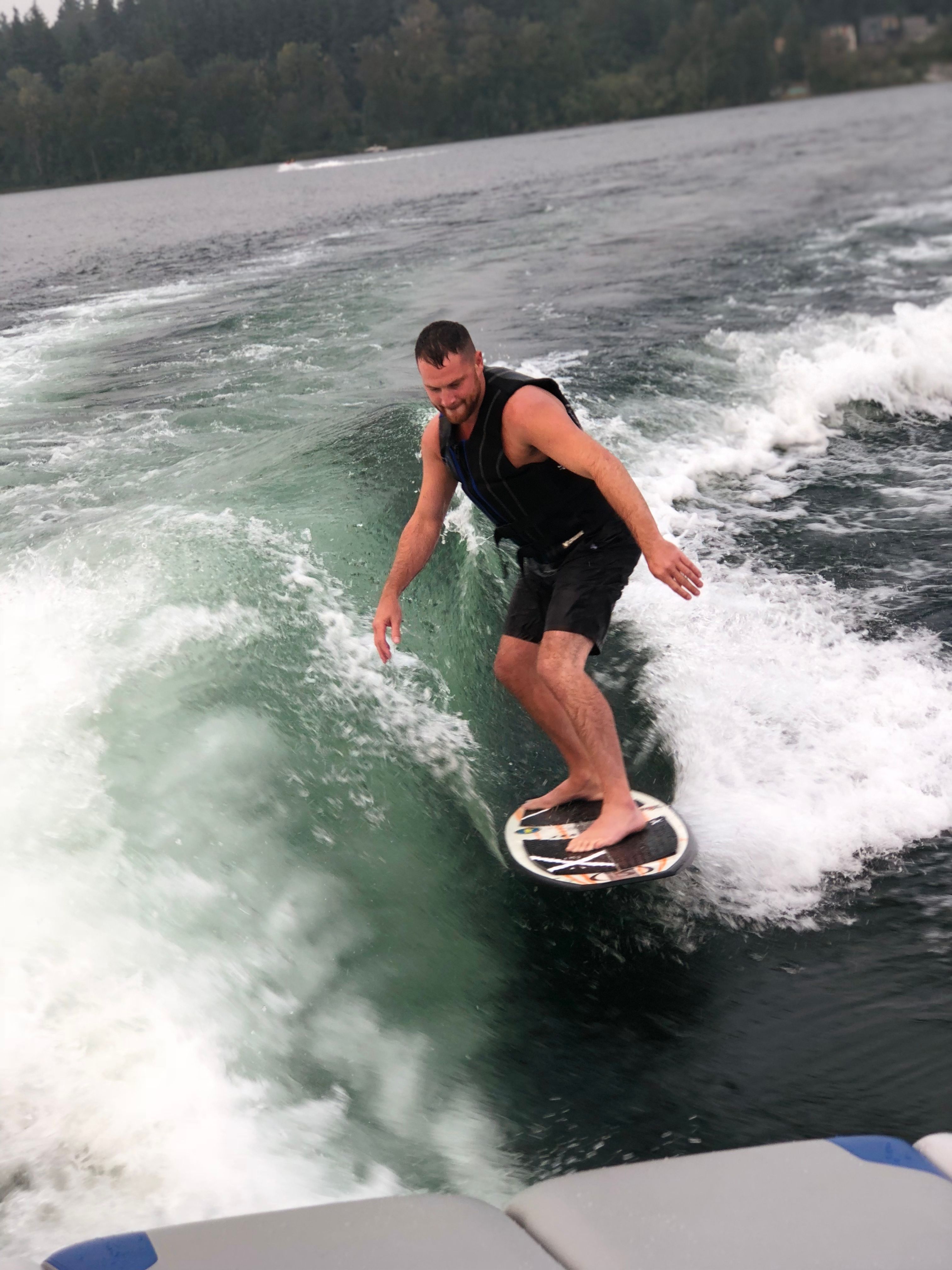 Man surfing wave behind boat, wearing life vest.