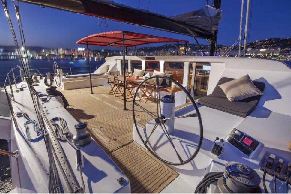 Luxurious 2003 VPLP 77 yacht deck at night with elegant seating and city lights.