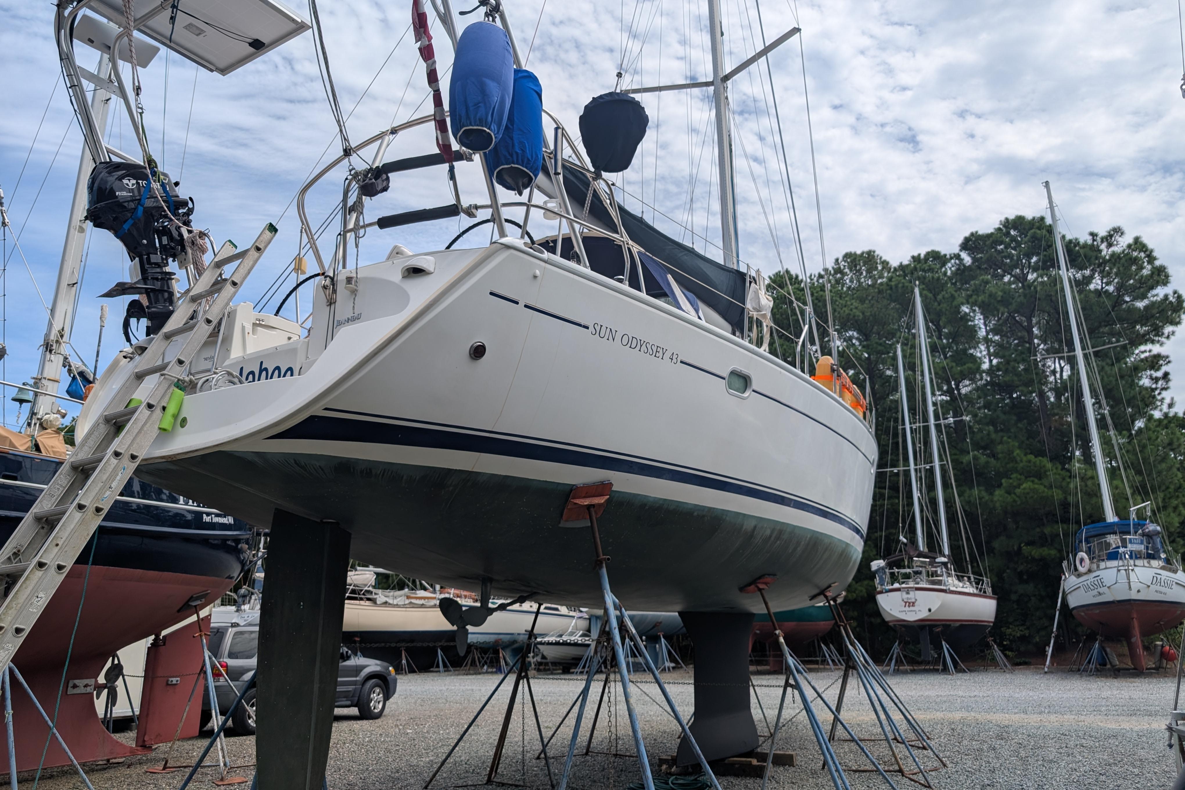 2001 Jeanneau 43 Sun Odyssey sailboat on stands in a boatyard, surrounded by trees.
