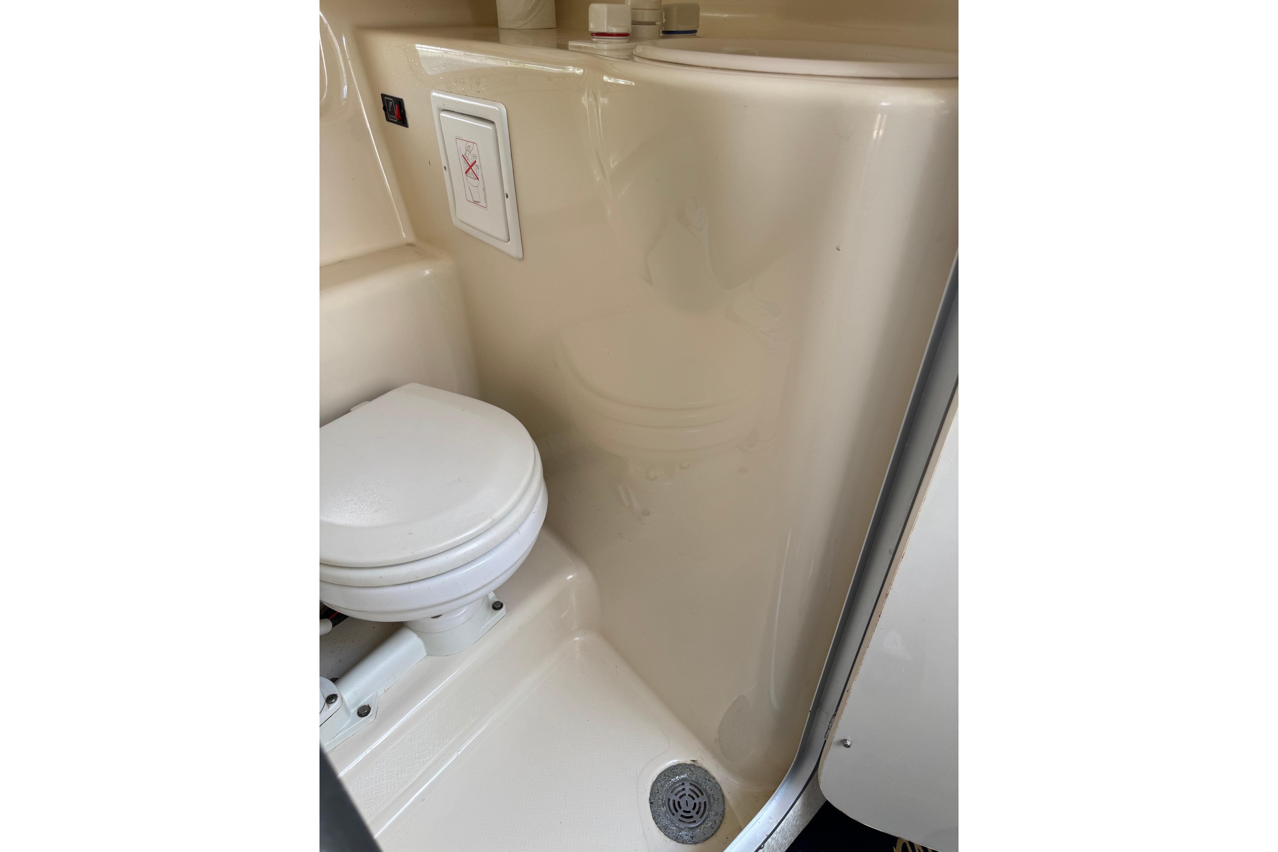 Compact bathroom in a 2000 Maxum 2400 SCR boat, featuring a toilet and shower area.