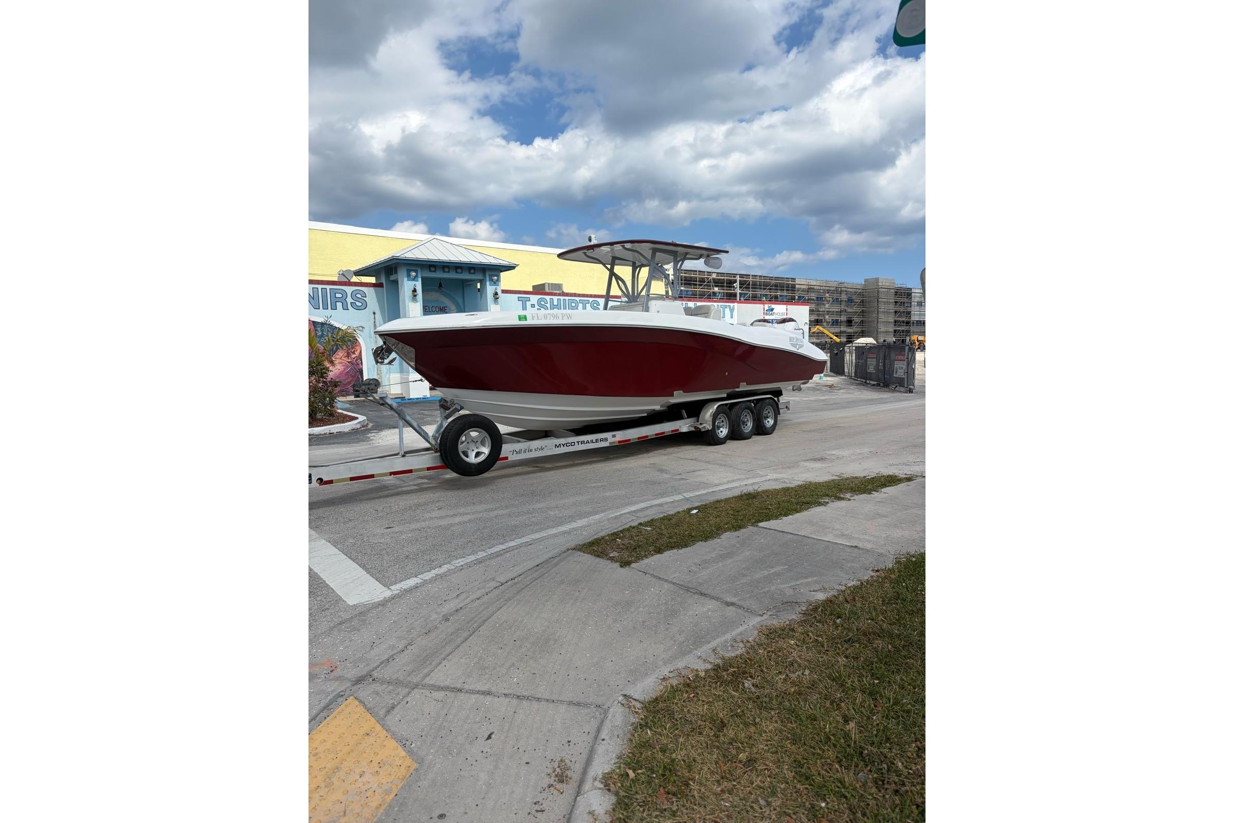 2015 Deep Impact 33 boat on trailer, parked near colorful building under cloudy sky.