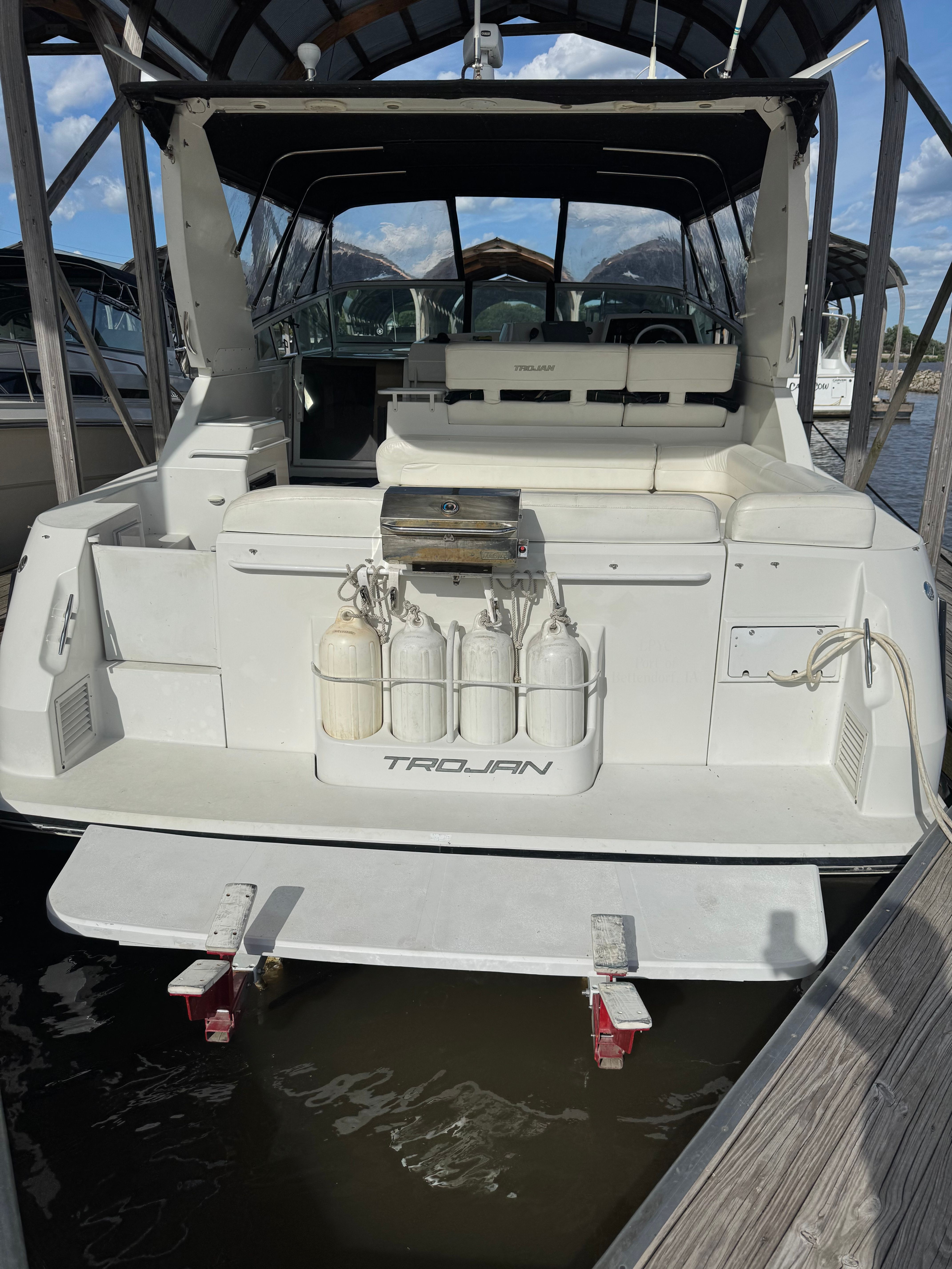 Rear view of a white motor yacht with seating area and fenders, docked in water.