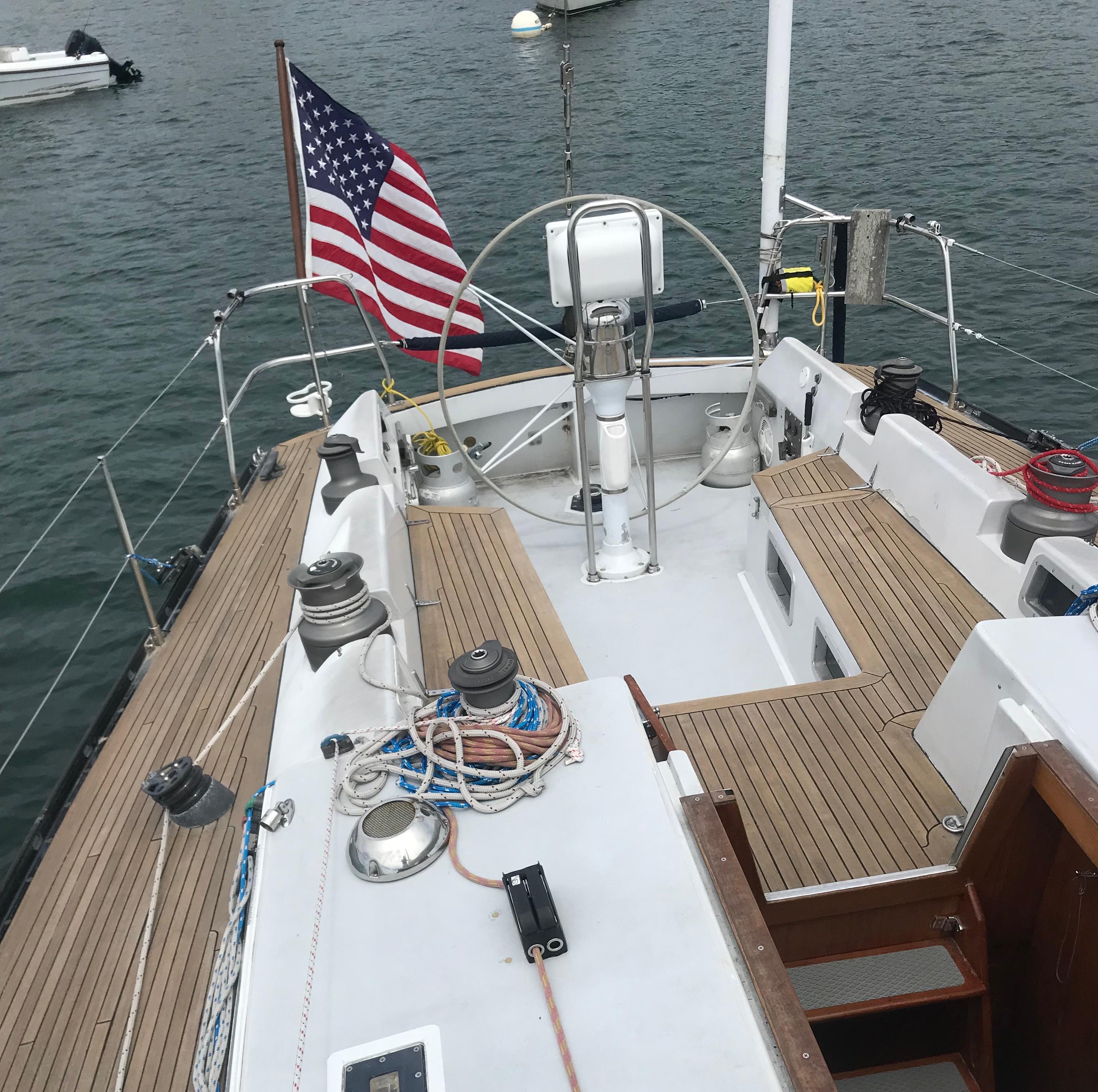 1986 Baltic Custom Farr 44 sailboat deck with American flag, wooden seating, and steering wheel.