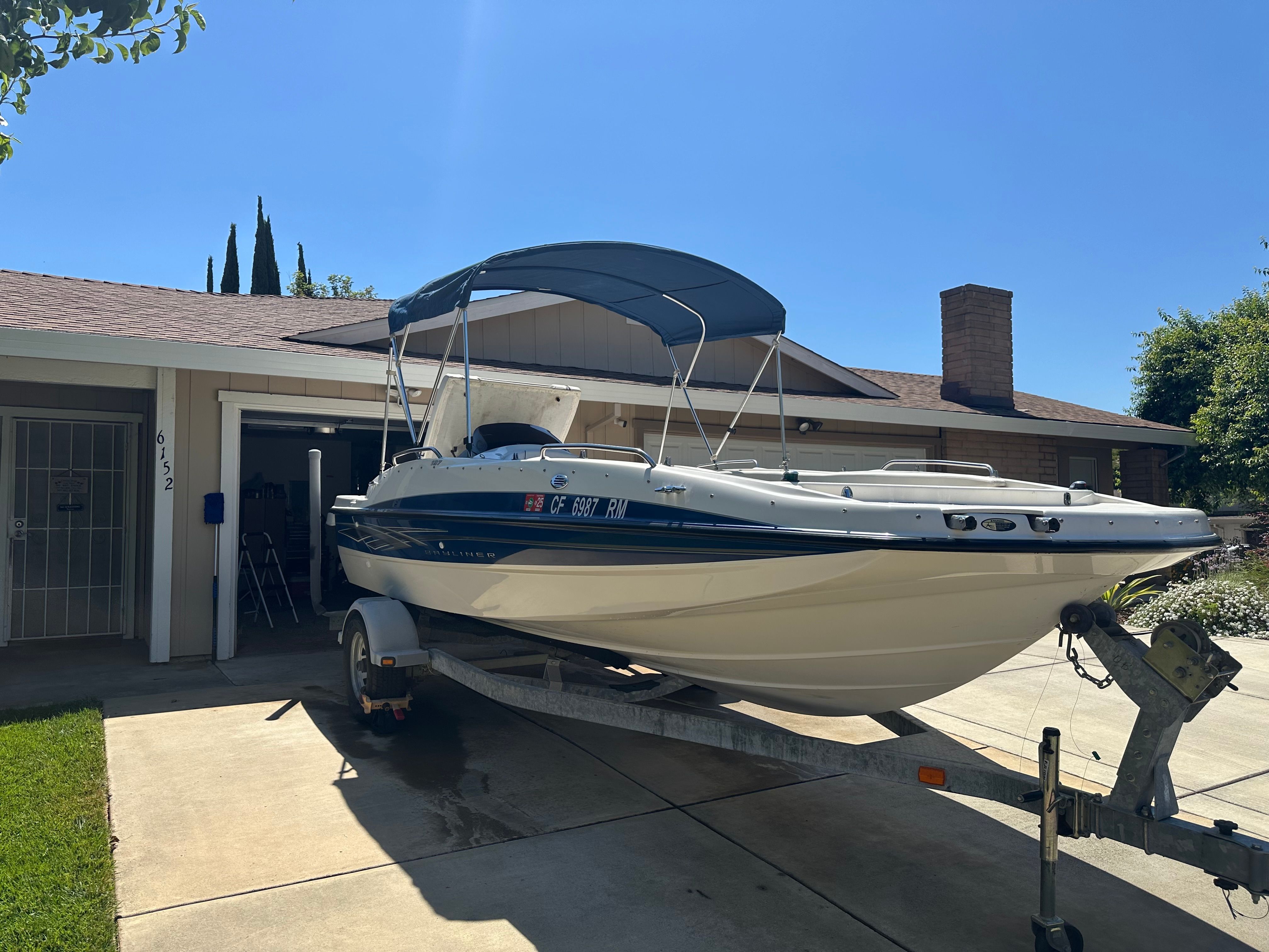 A Bayliner boat on a trailer in front of a garage.