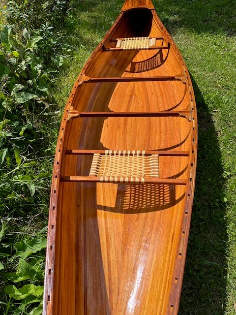 A handcrafted cedar strip canoe with woven seats on grass.