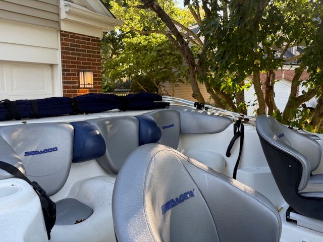 2004 Bombardier Challenger boat with blue and gray seating, parked near a brick house.