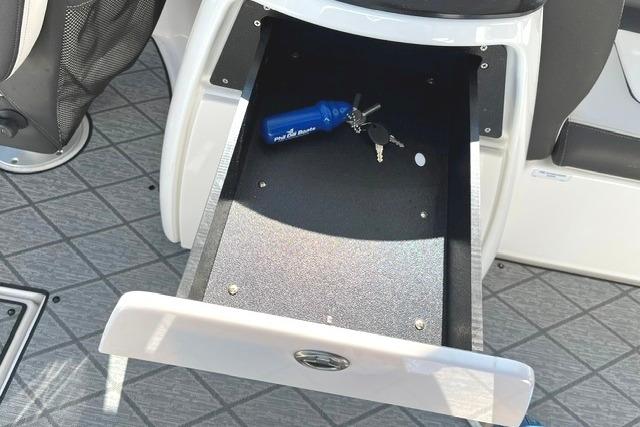 Open storage compartment in 2021 Yamaha Boats 275SD with keys and blue item inside.
