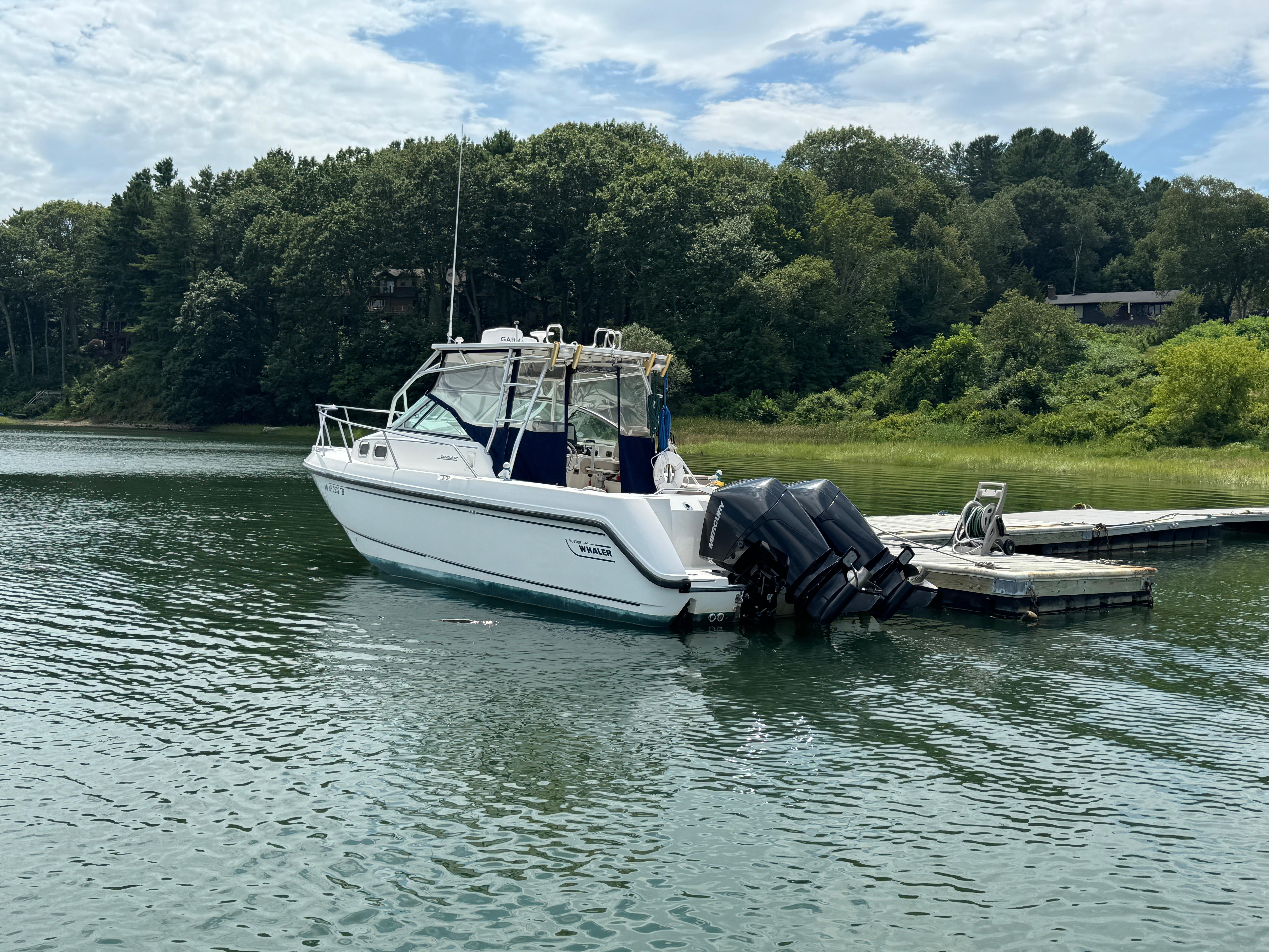 1999 Boston Whaler 28 Conquest boat docked on calm water, surrounded by lush greenery.