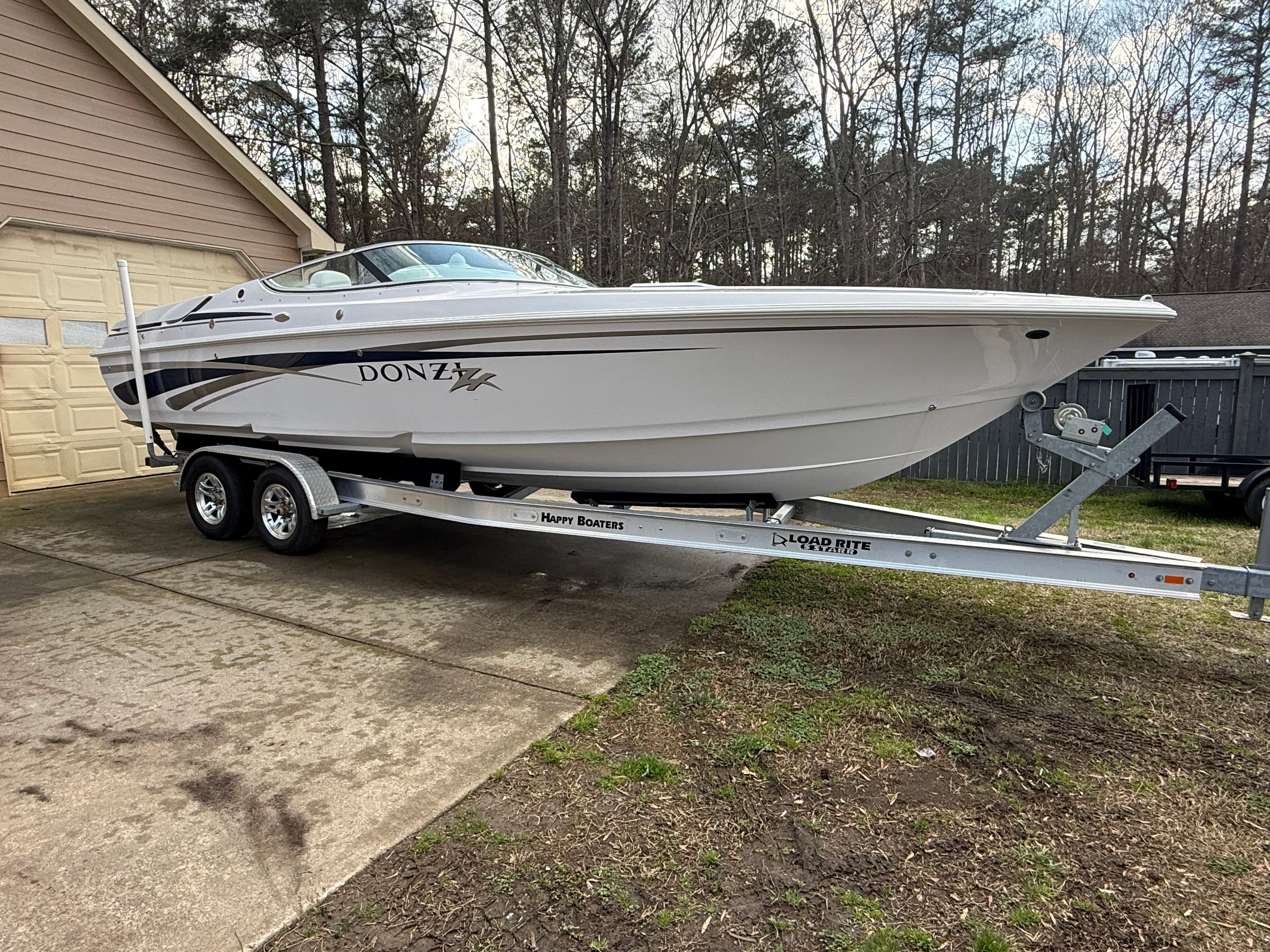 A white 2003 Donzi 28 ZX boat is on a trailer in a driveway.