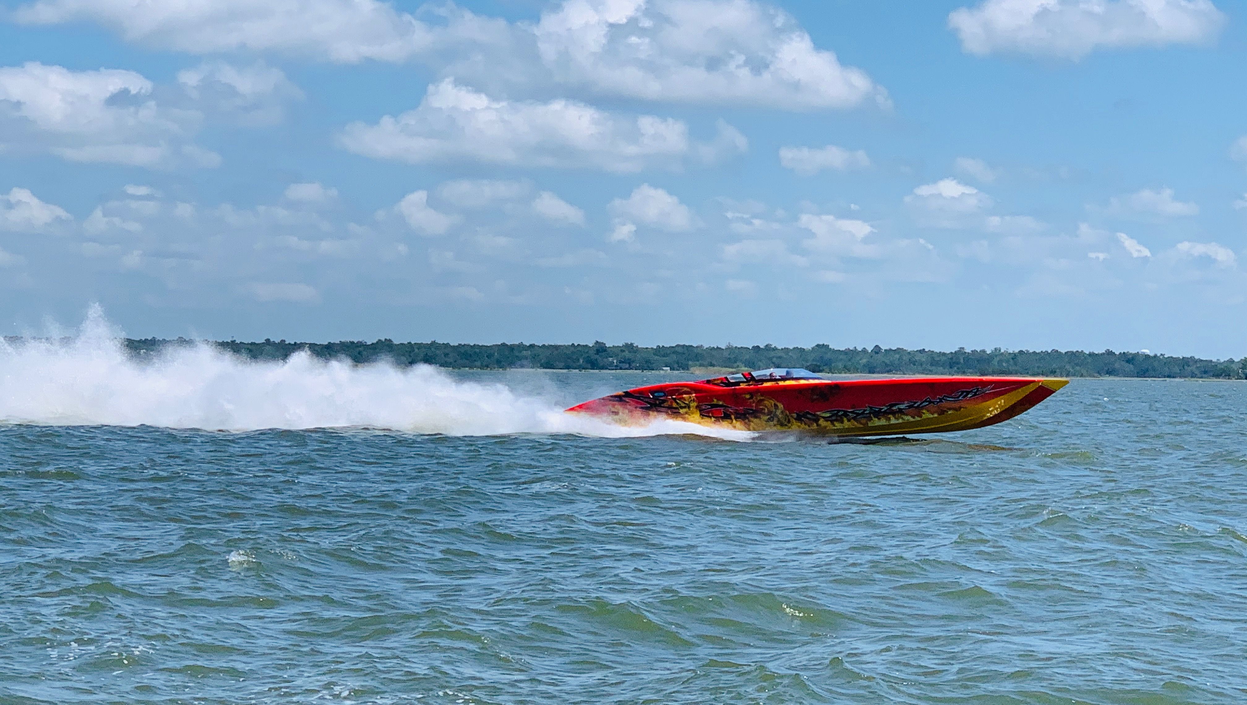 A red high-speed boat races across the water under a blue sky.