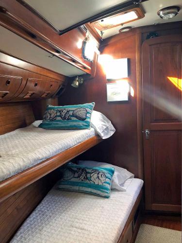 Interior of a yacht with two bunk beds, wooden walls, and fish-themed pillows.